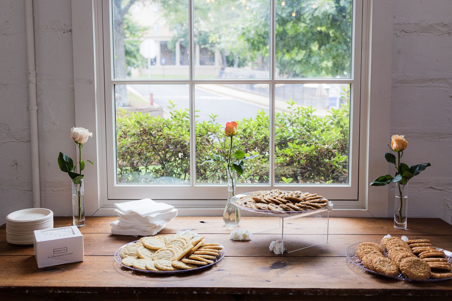Bright window view with decorative items arranged on a wooden table against white painted brick wall.