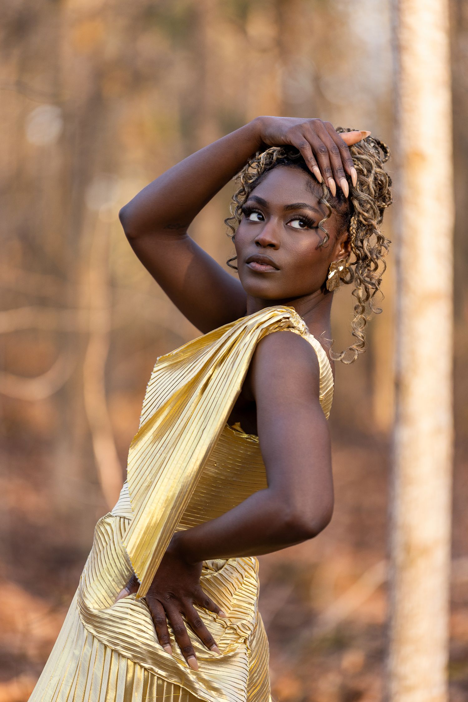 Fashion portrait in pleated yellow gown with golden afternoon light in wooded setting.