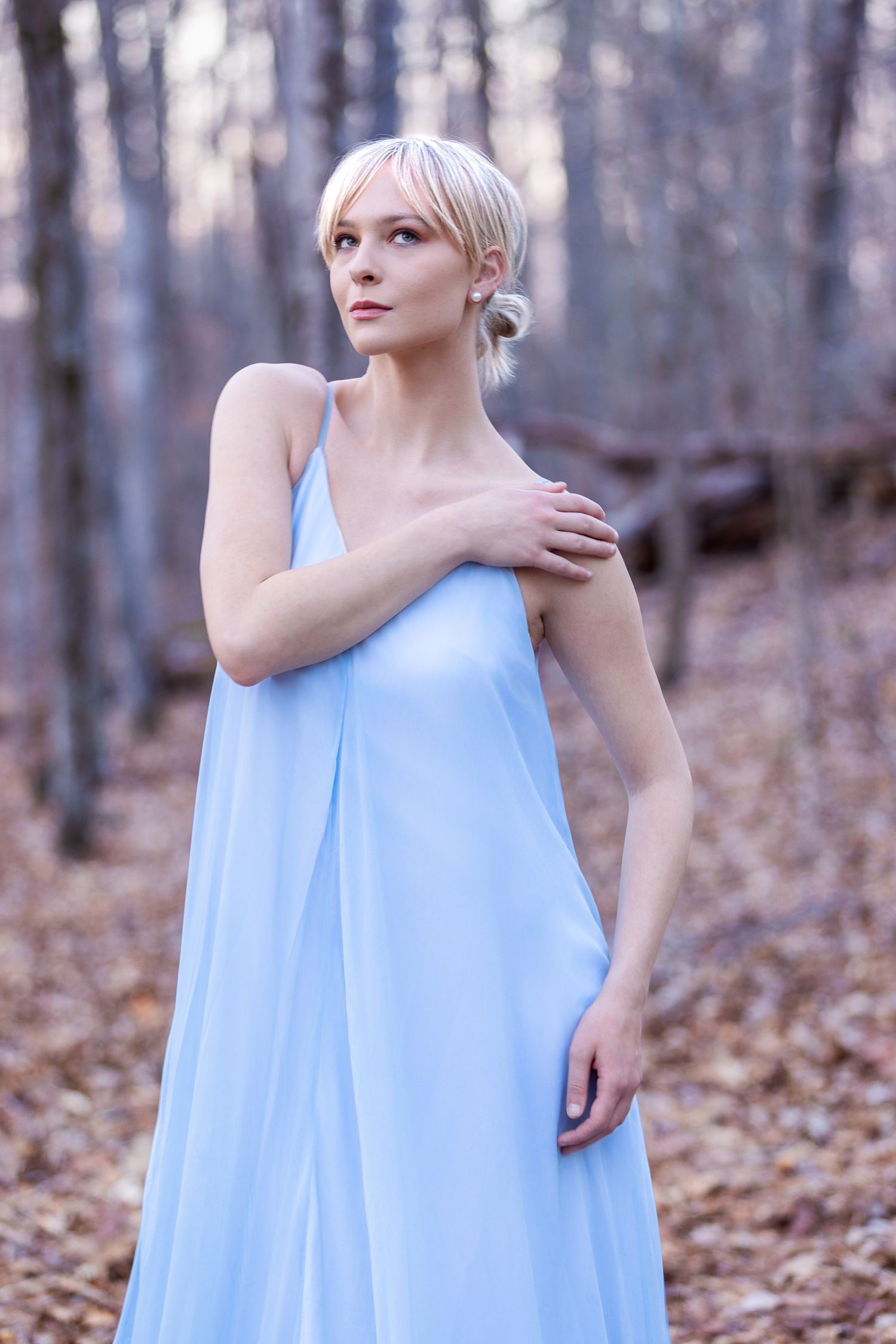 Ethereal light blue flowing dress captured in forest during autumn season.