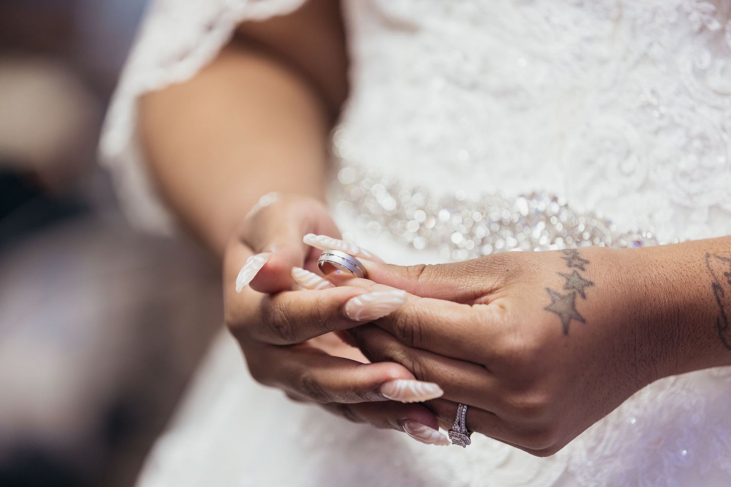 Close-up of hands exchanging wedding rings during ceremony with lace dress detail.