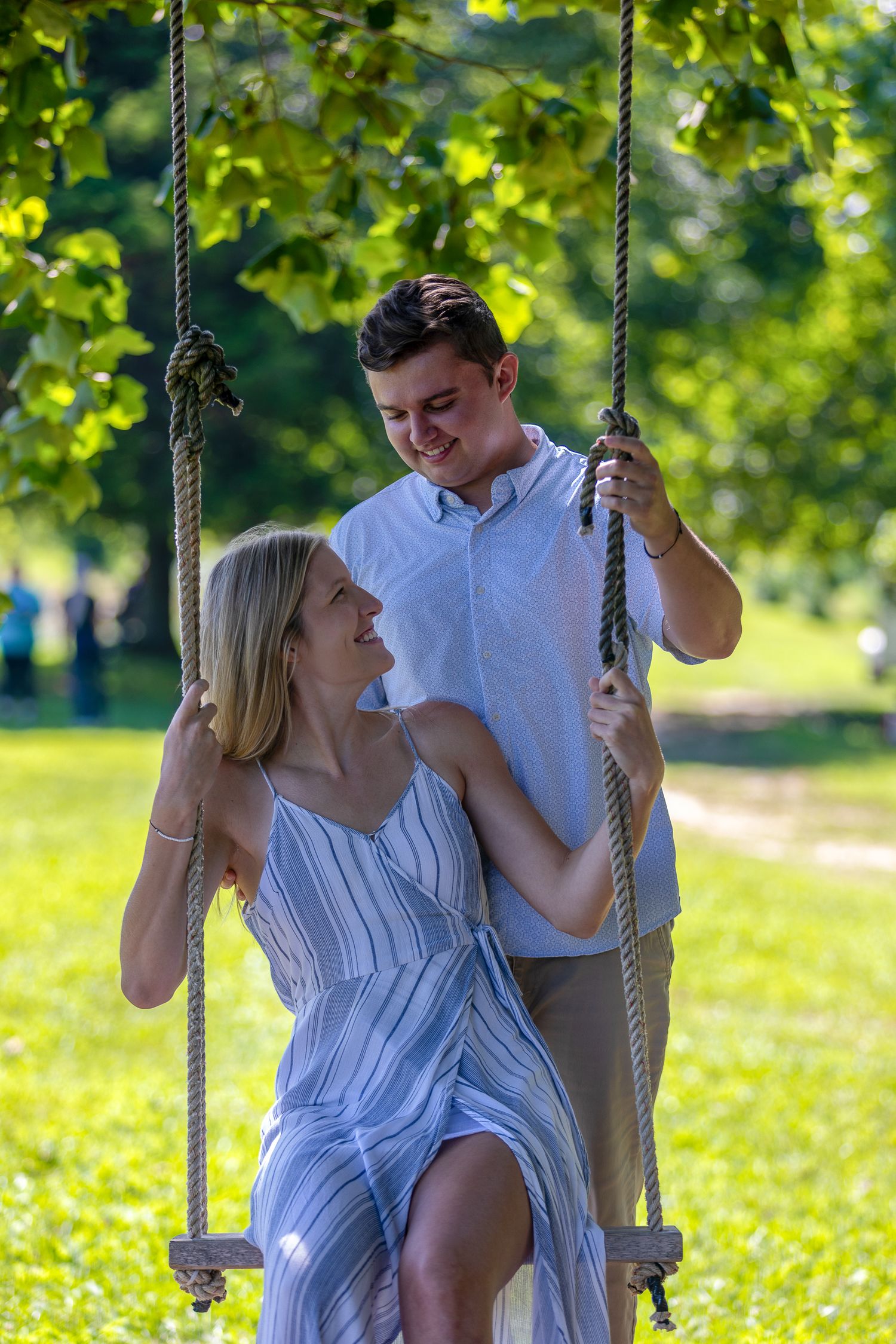 Couple shares romantic moment on wooden swing in sunlit garden setting.