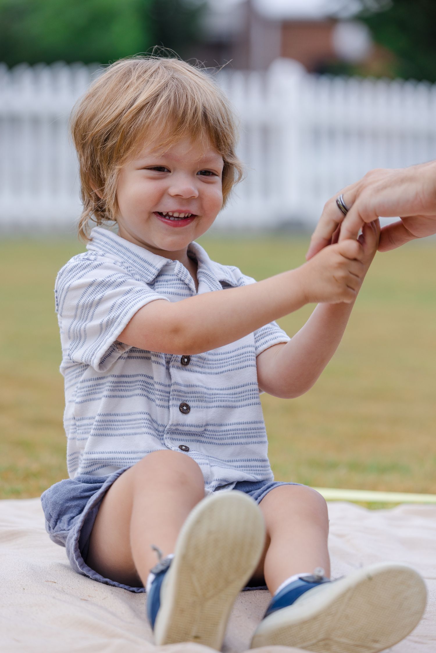 Playful toddler in striped outfit laughing while sitting on blanket outdoors.