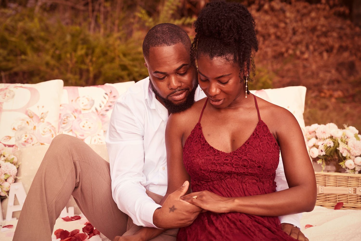 An intimate outdoor portrait of a couple sitting close together on white cushions.