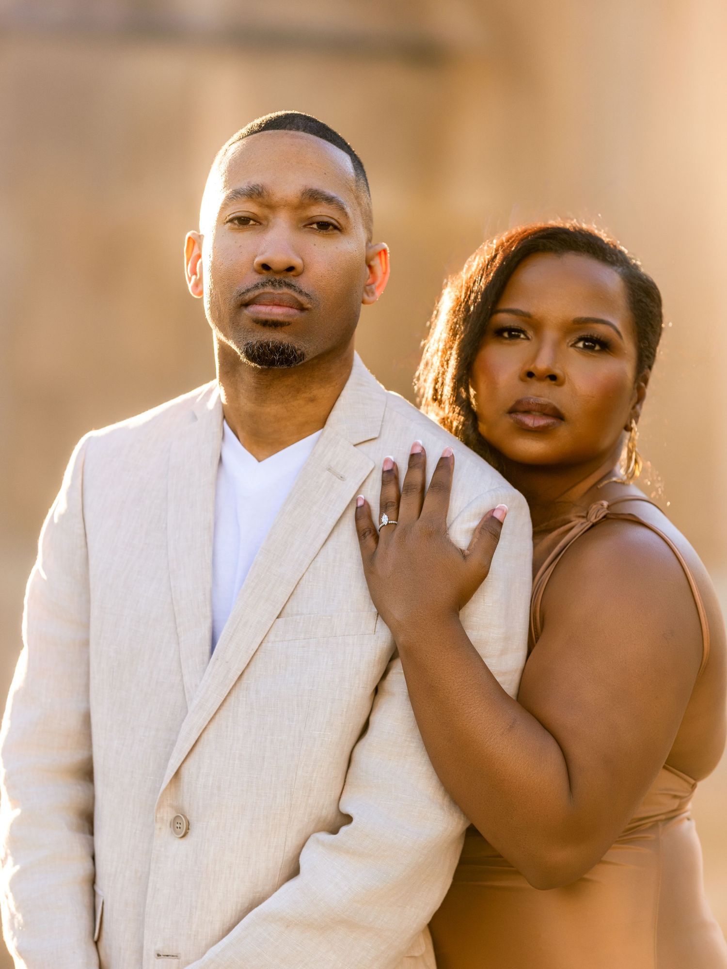 A couple poses intimately in formal attire during sunset for their engagement photos.