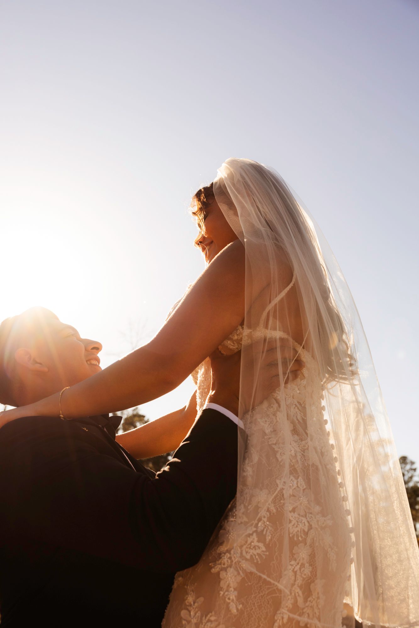 Romantic backlit wedding photo showing lace veil detail against bright sunlight.