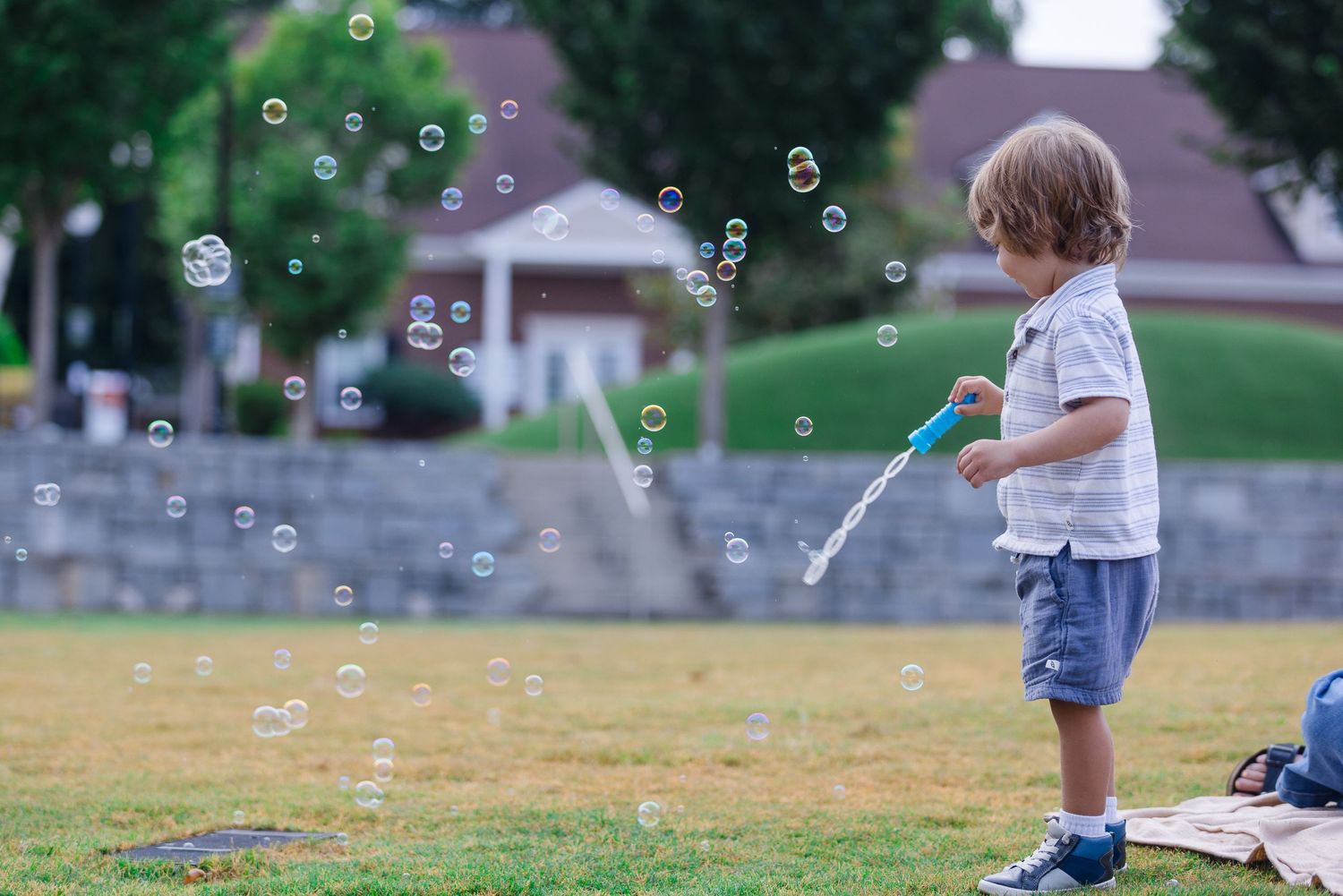 Young child plays with soap bubbles on grassy lawn during summer day.