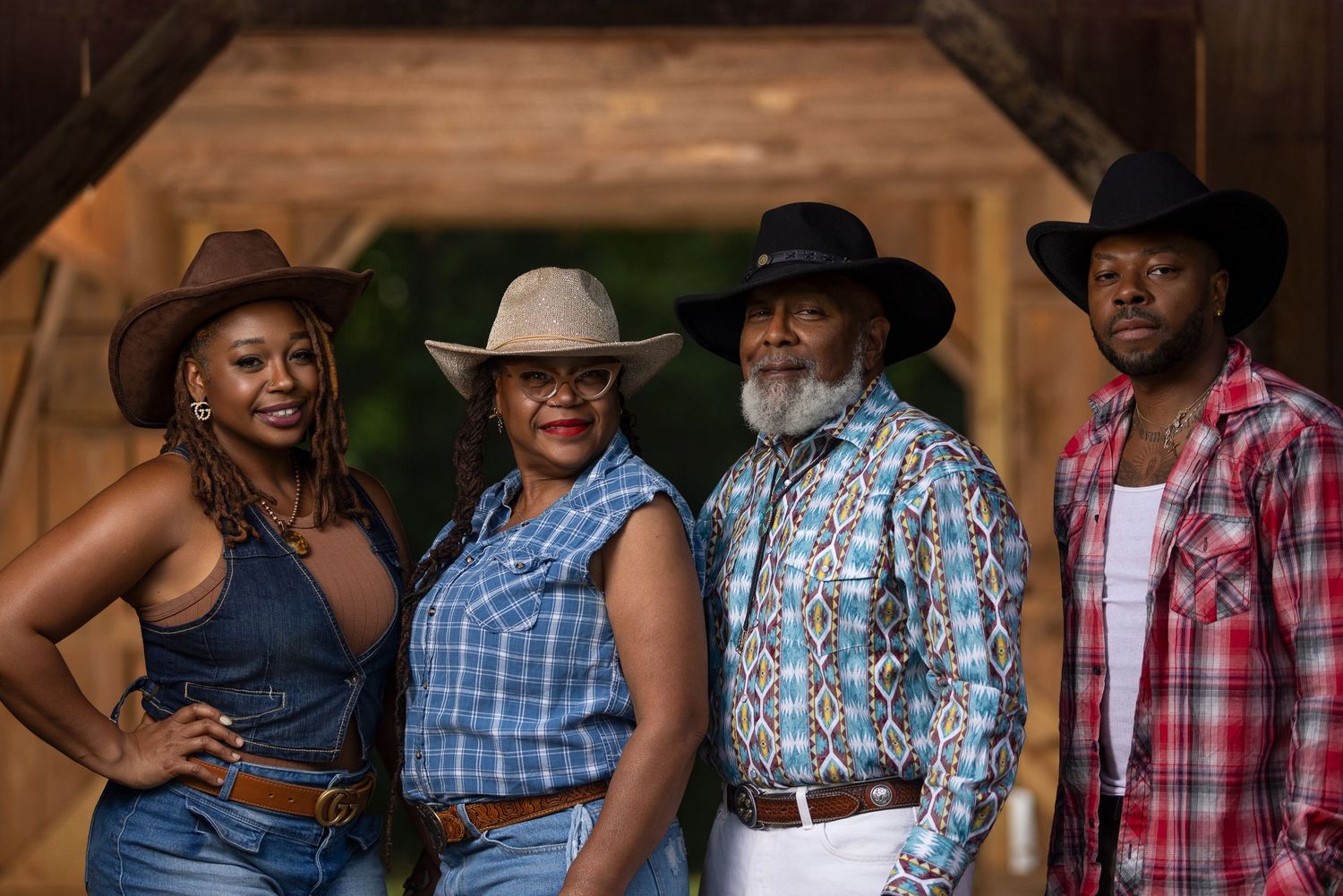 Group of four people in western attire pose together in rustic wooden barn doorway.