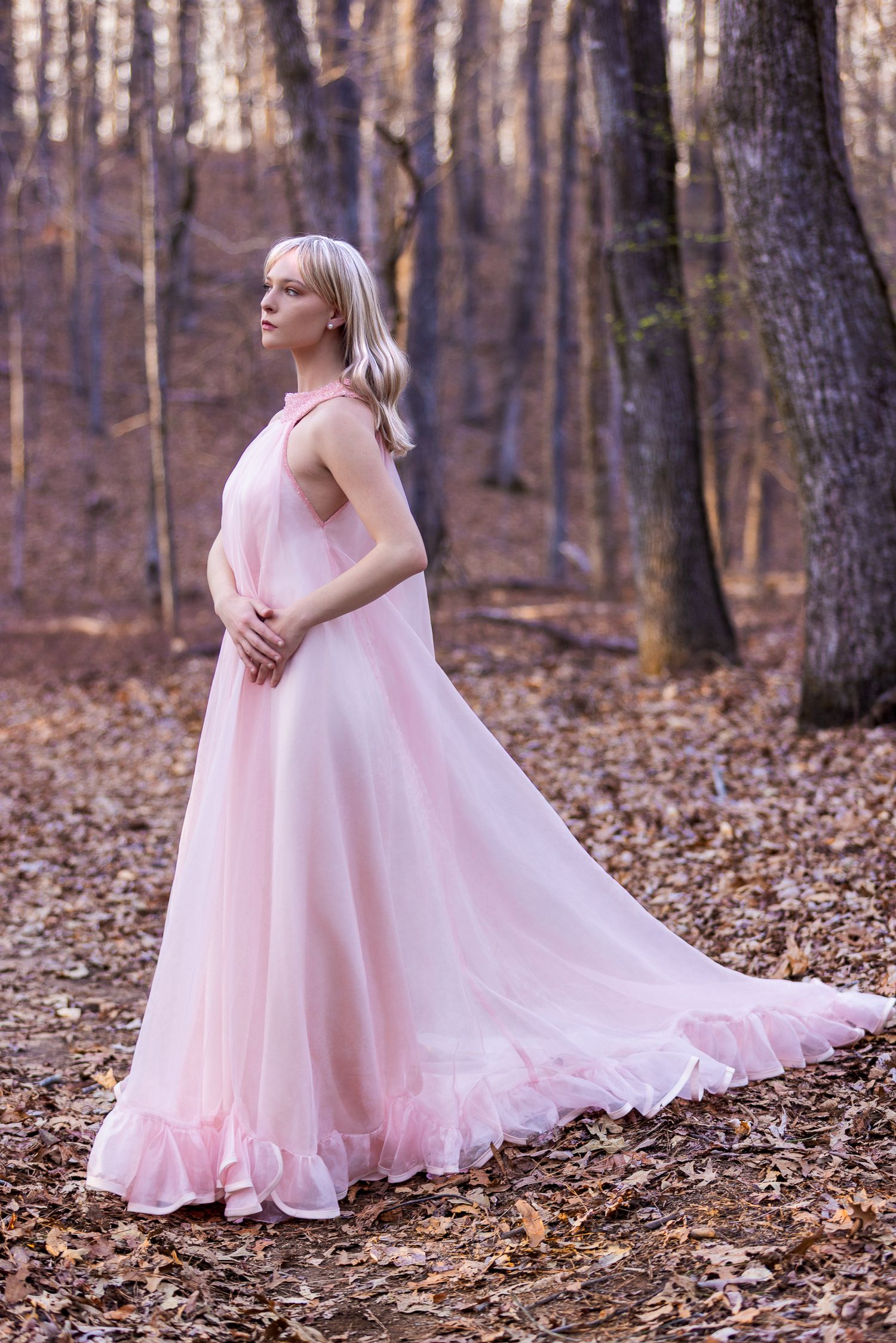 Soft pink chiffon gown captured against fallen leaves in a wooded setting.