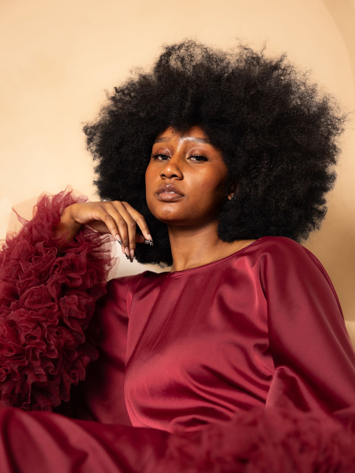 Artistic portrait featuring flowing burgundy dress against warm beige background.