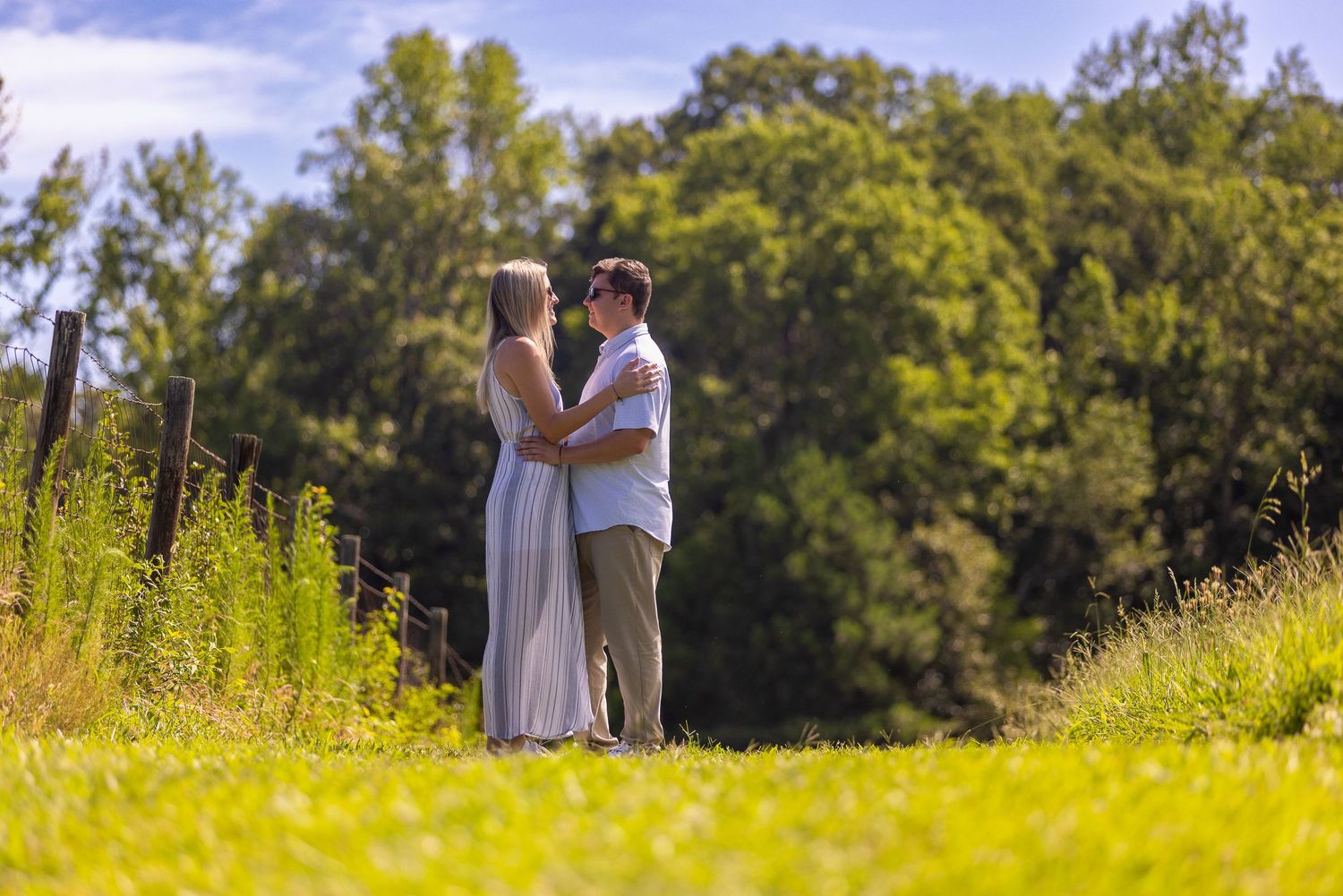 Silhouette of couple standing in golden sunlit field with trees in background.