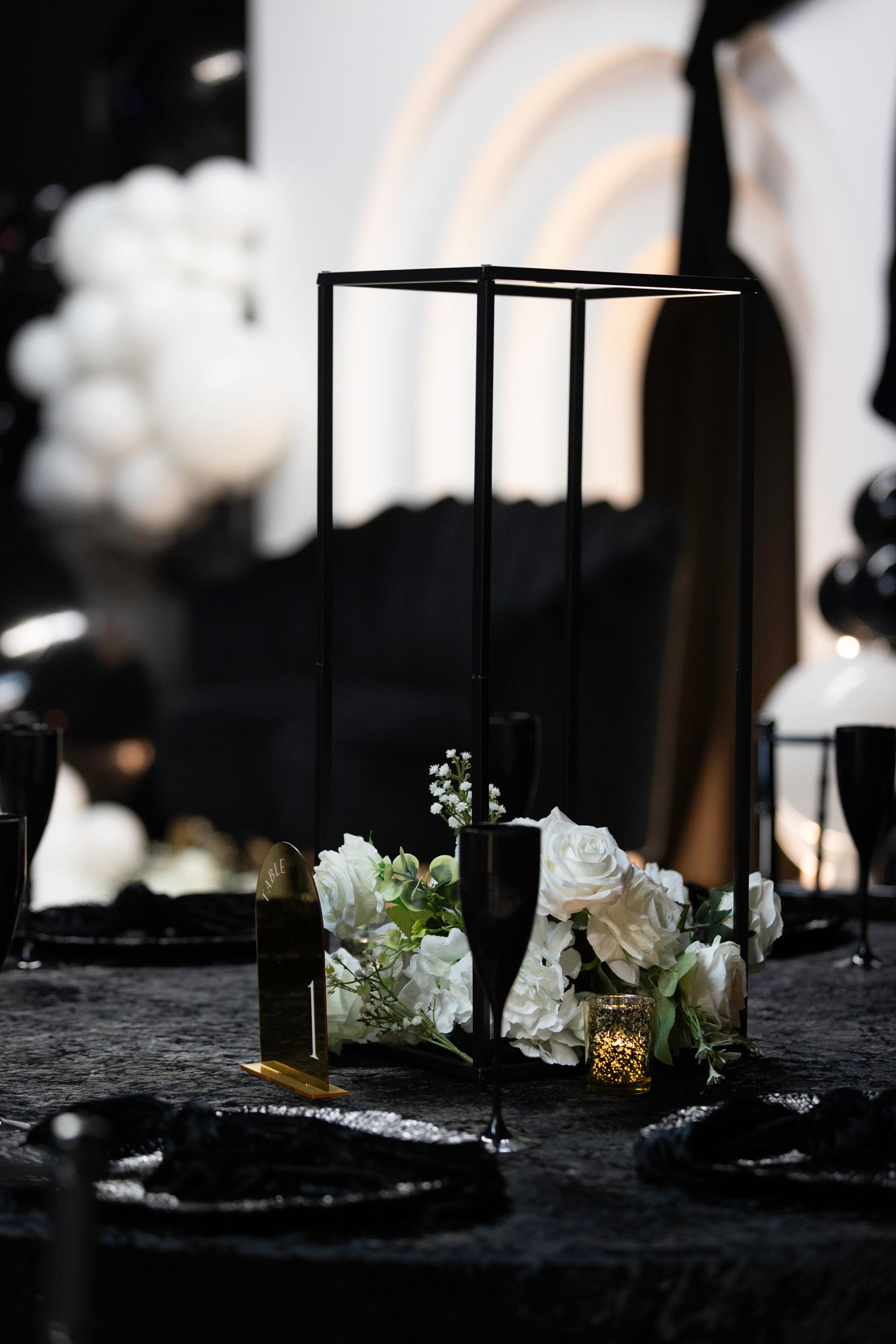 Modern black lantern decorations with white roses and candlelight in dark setting.