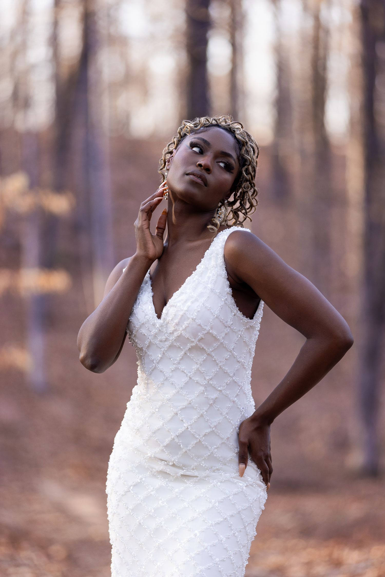 Fashion model wearing white textured gown poses gracefully in autumn woods.