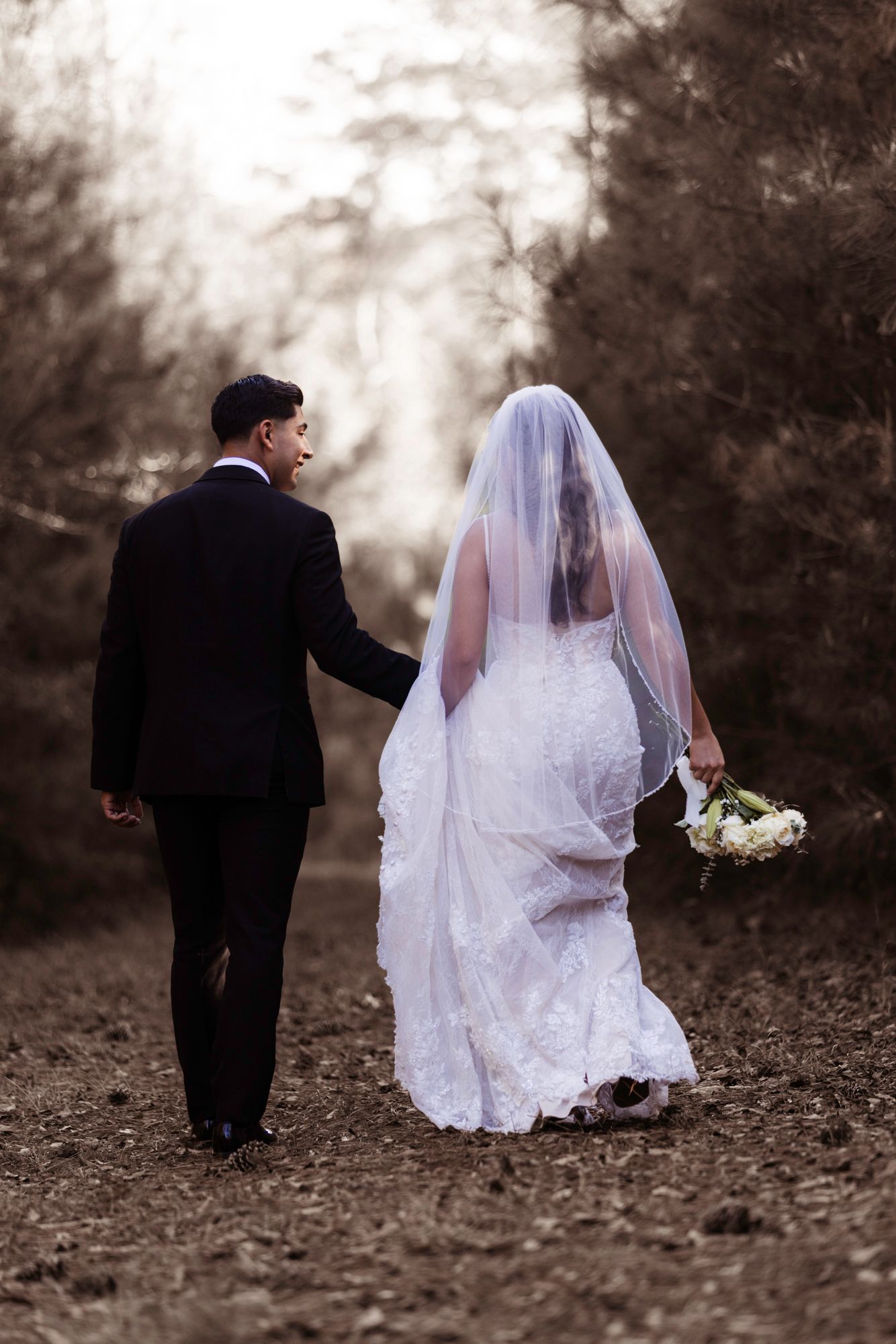 Wedding couple strolling down a misty woodland path with fall foliage in the background.