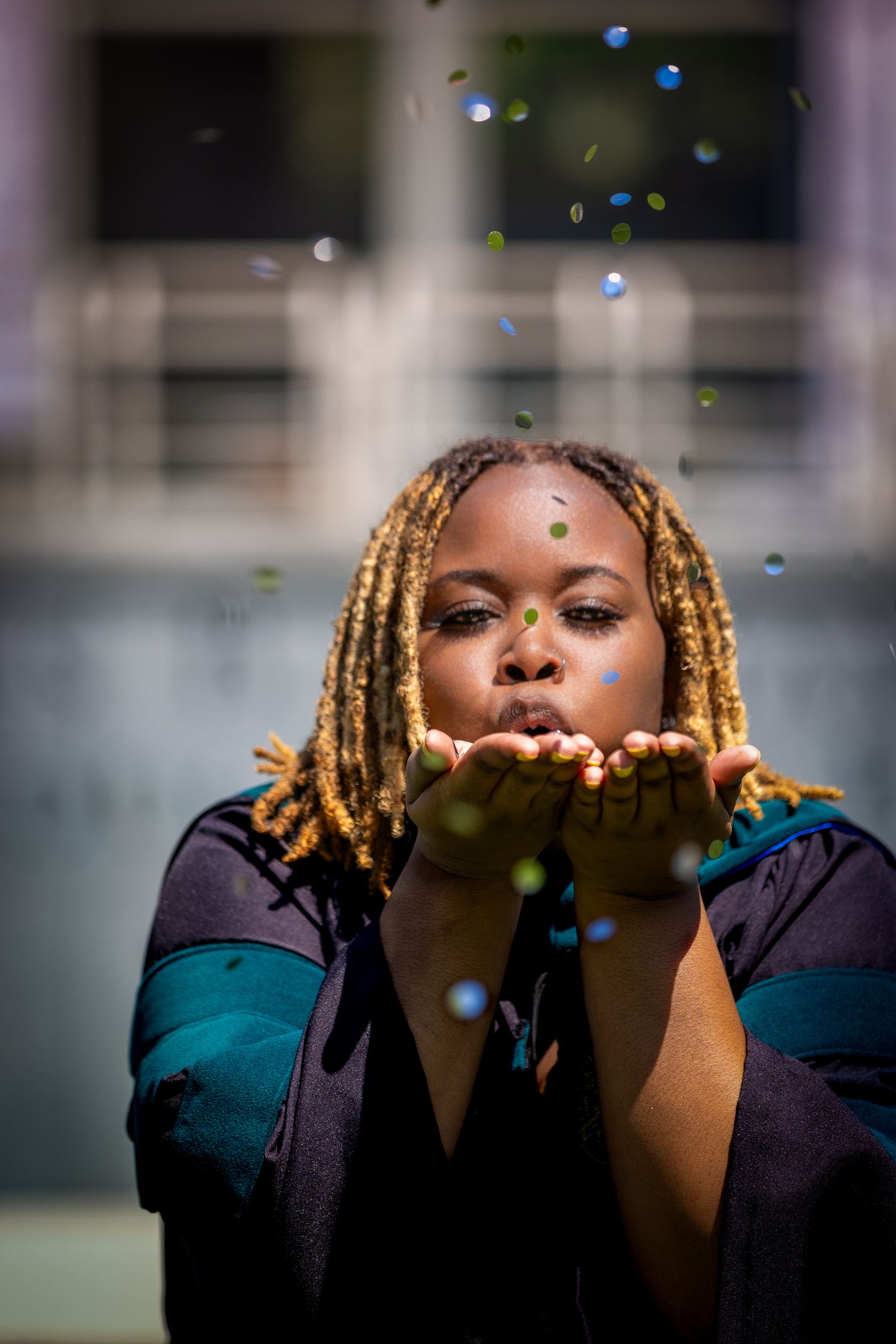 Graduate with blonde braids blows glitter in artistic graduation photo sequence.