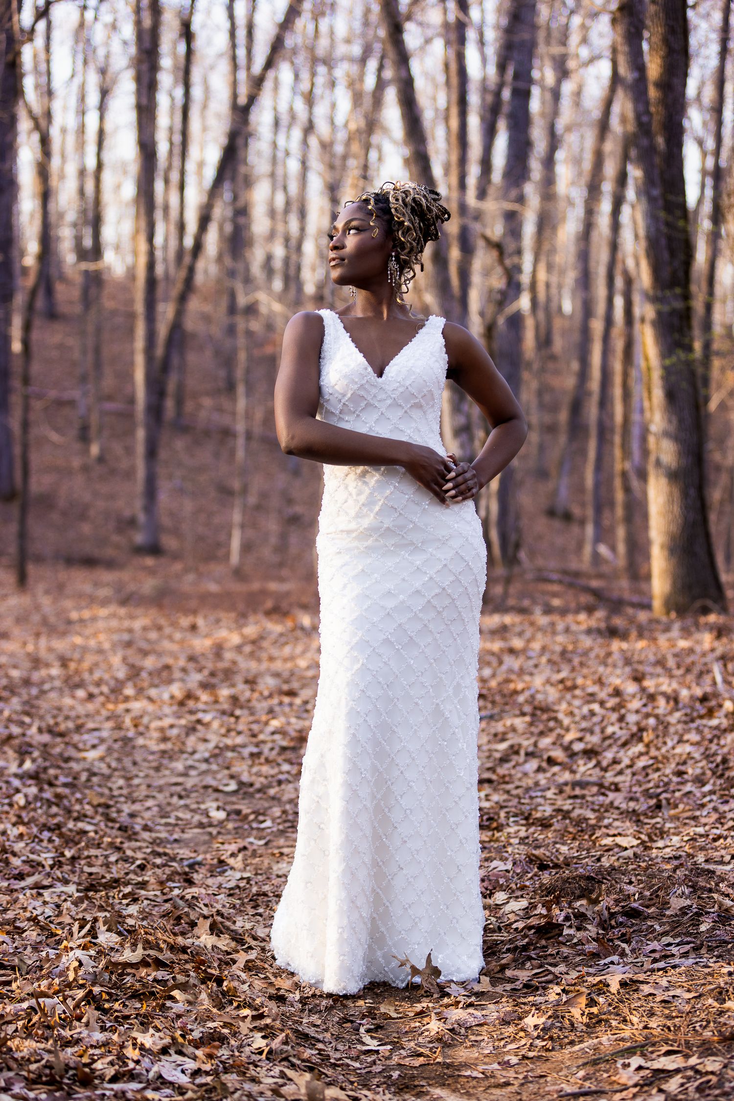 Full-length white wedding gown displayed in scenic fall forest setting.