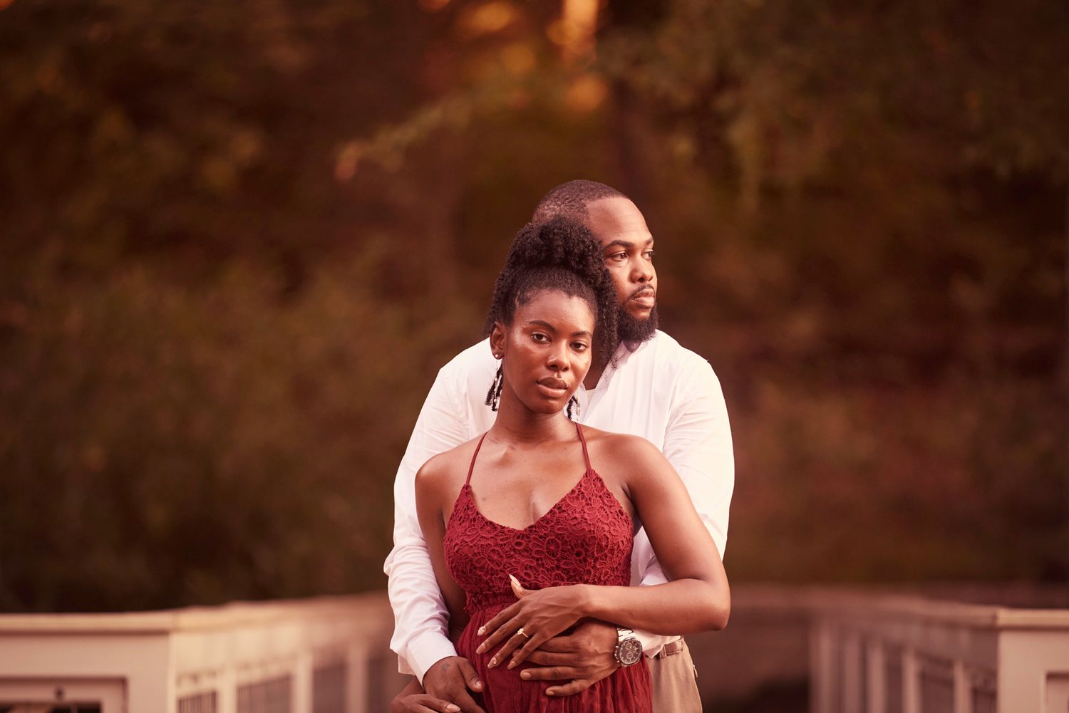 A tender embrace between a couple at golden hour with the person in a red dress leaning back.