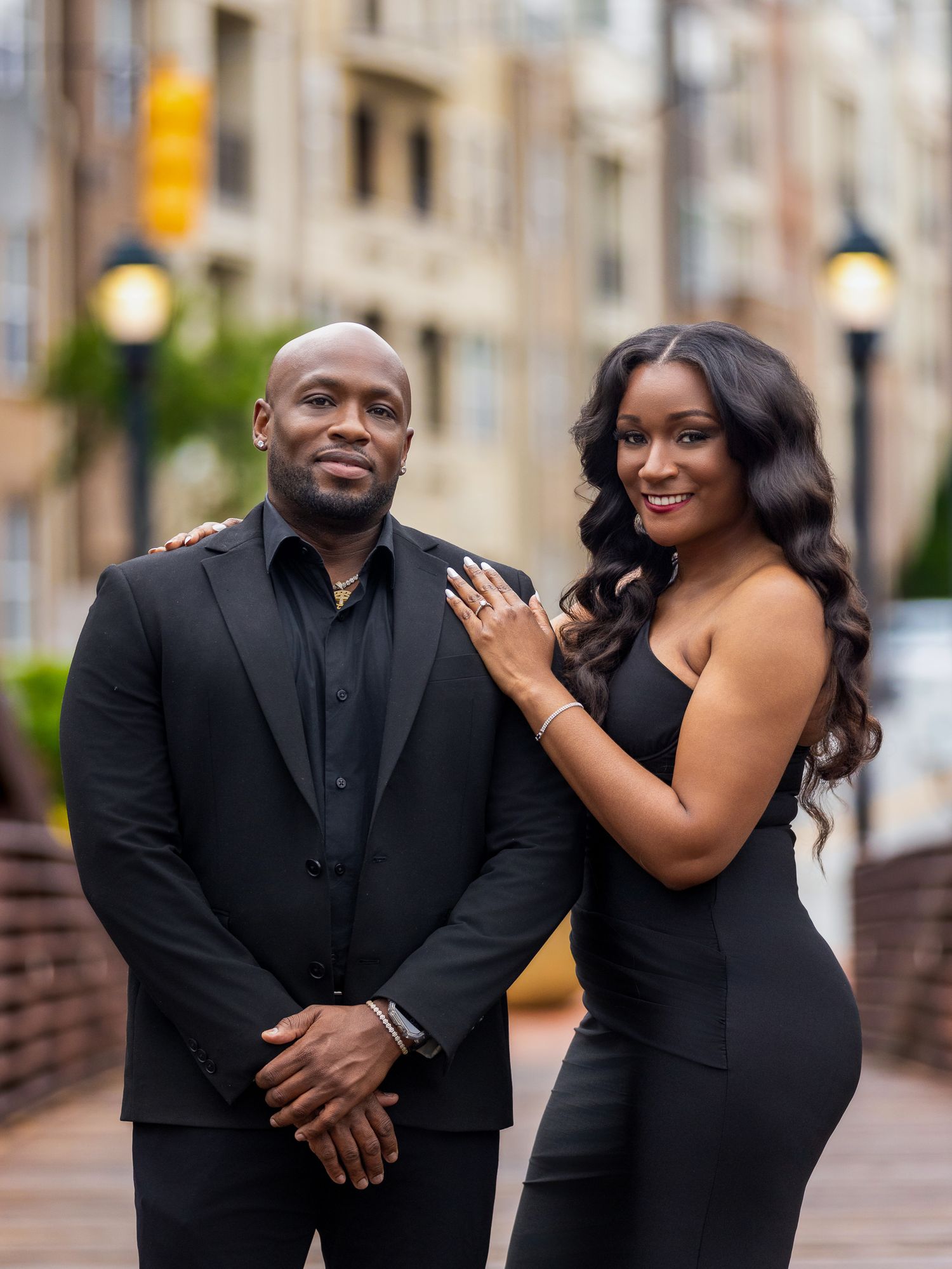 A couple poses in matching black formal wear during their urban engagement photoshoot.
