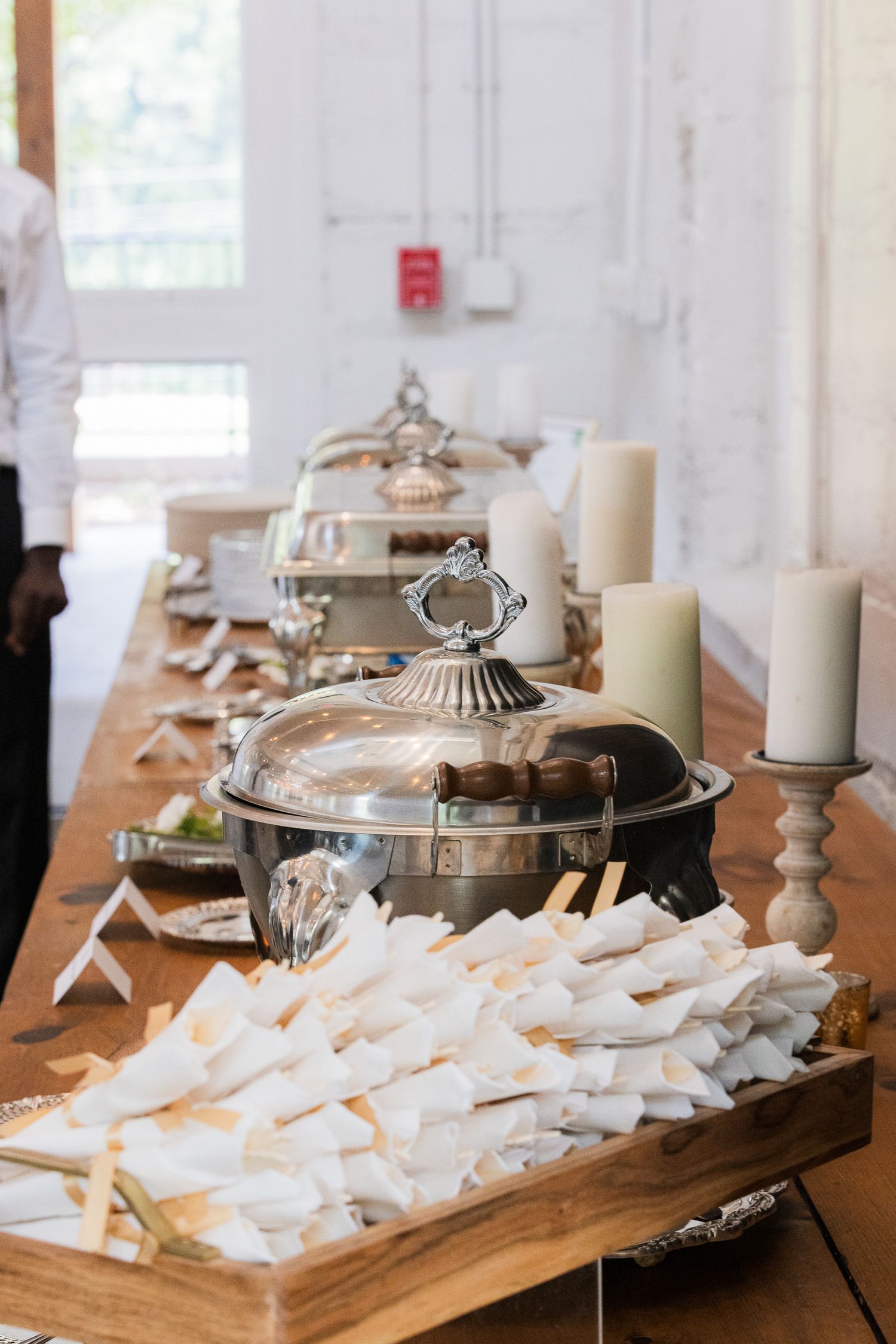 Elegant silver serving dishes and white candles arranged on wooden serving board.
