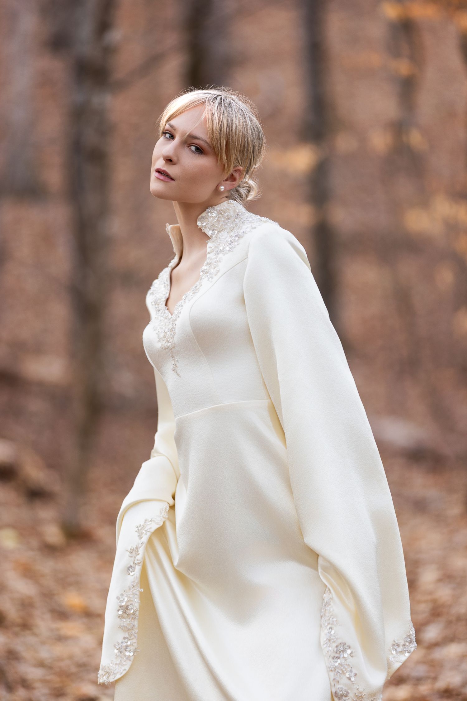 Elegant white lace wedding dress with flowing sleeves photographed in autumn forest setting.