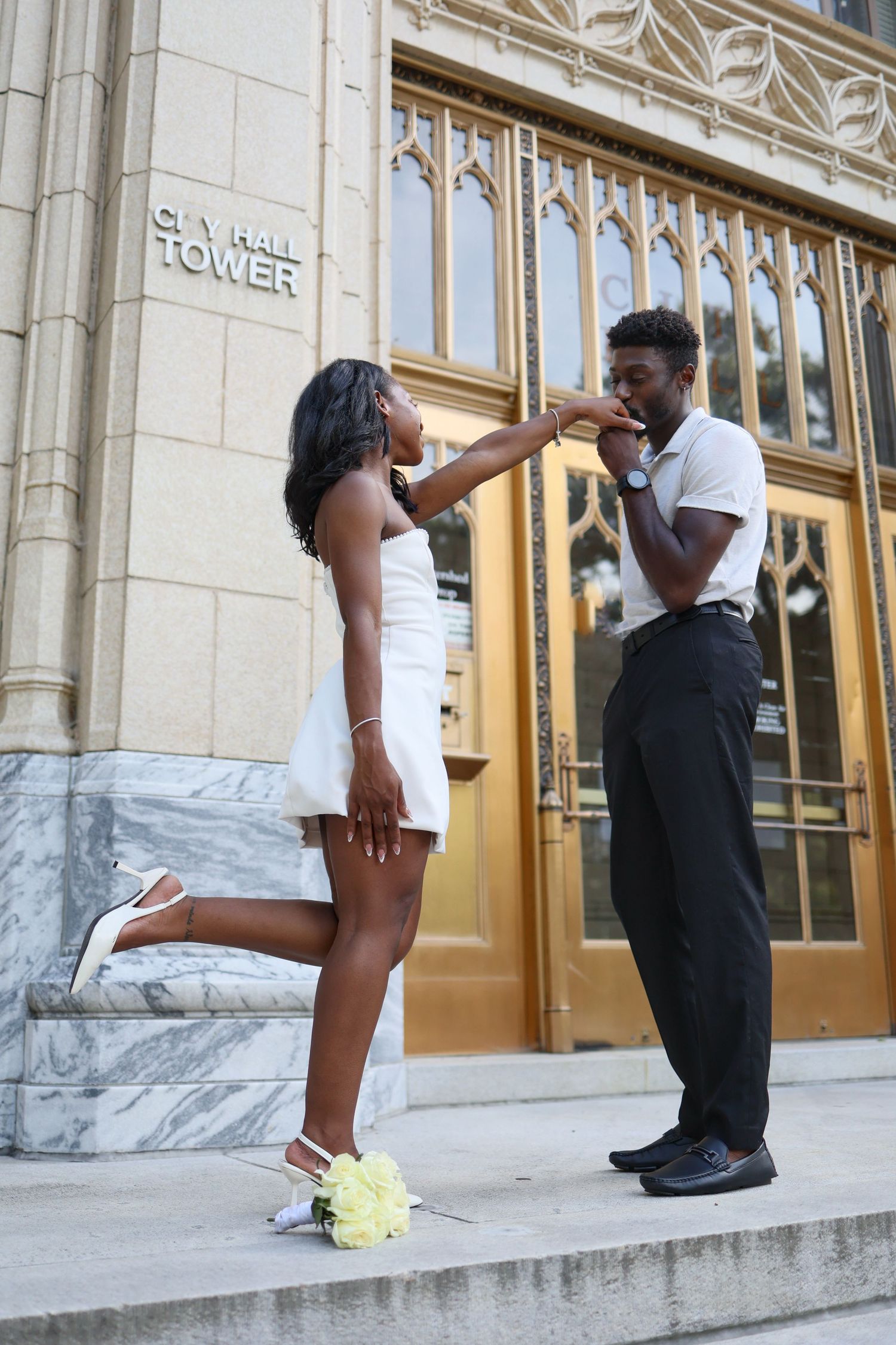A couple in formal wear shares a romantic moment on City Hall Tower steps, man kissing womans hand.