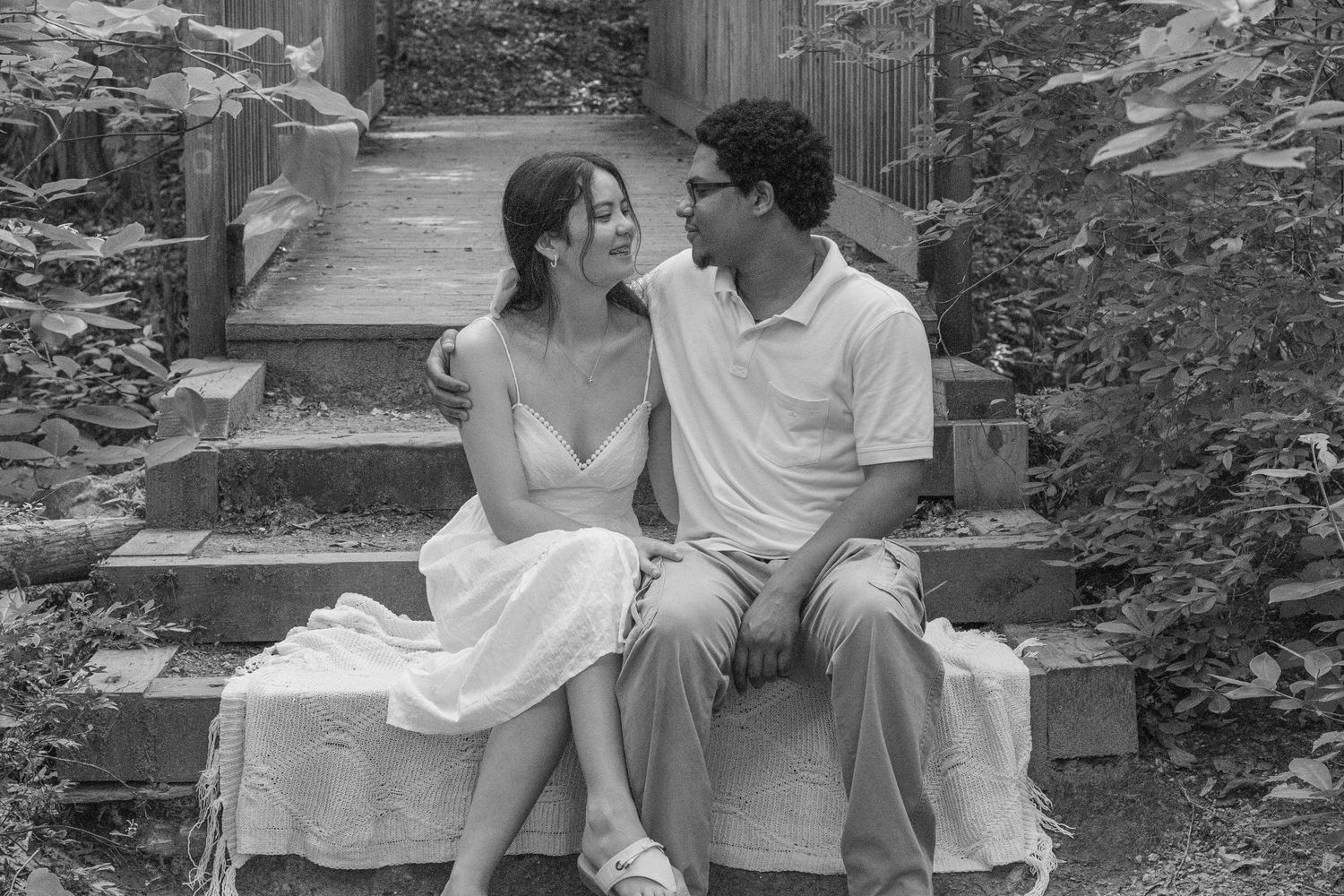 Black and white photo of a young couple sitting on stone steps sharing a romantic moment.