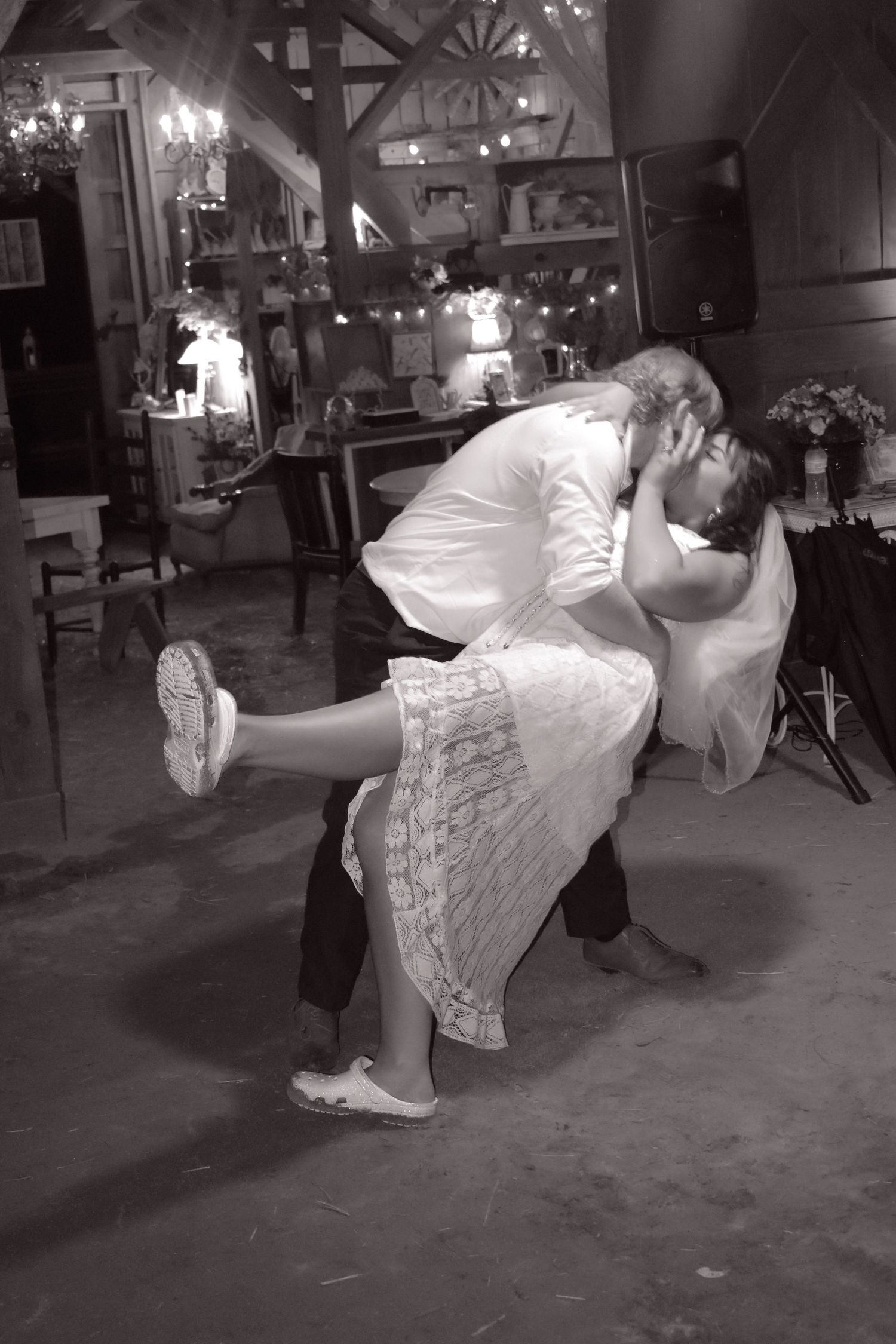 Black and white photo of groom dipping bride during first dance in a rustic barn reception venue.