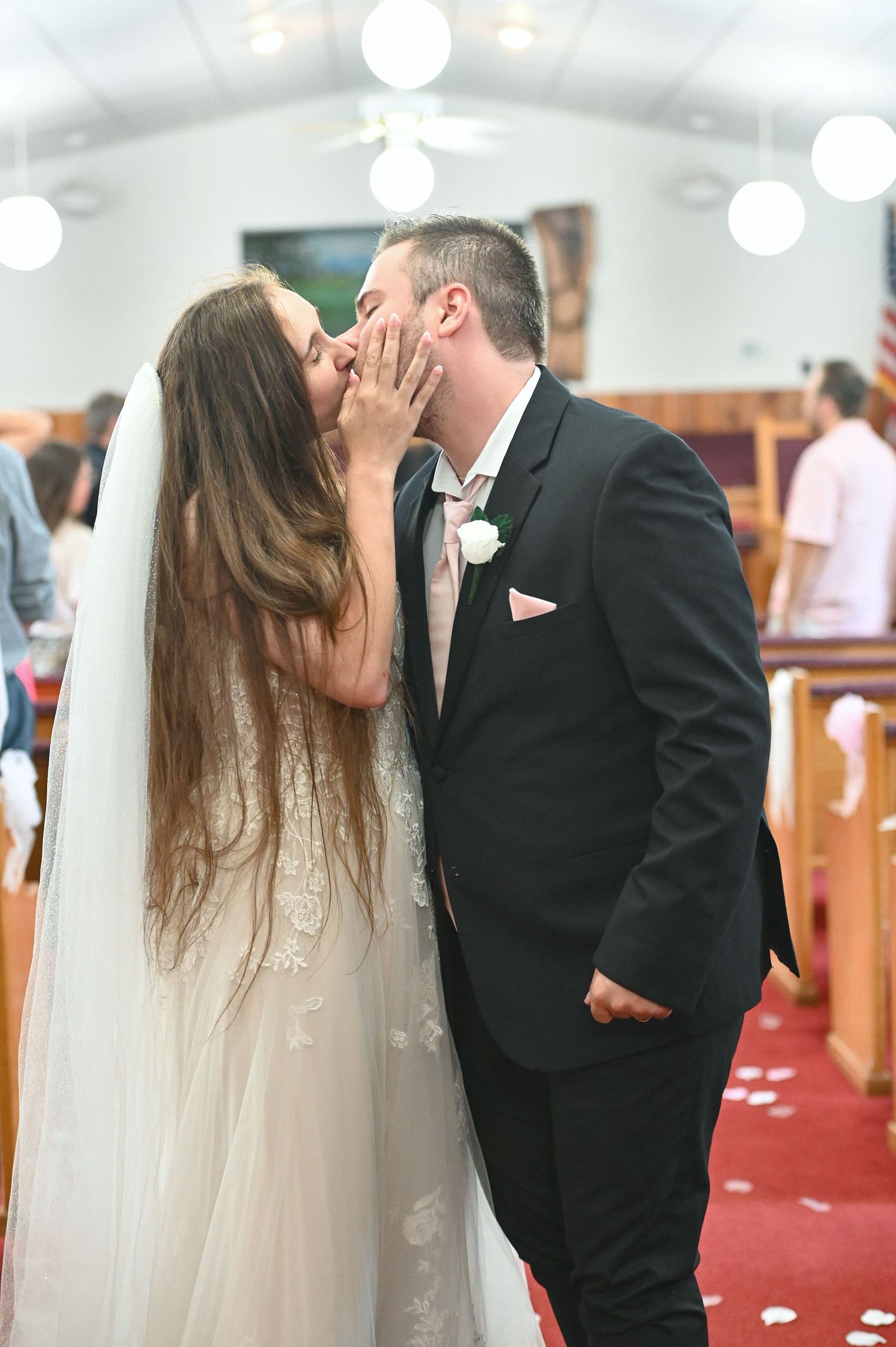Bride and groom share first kiss at church wedding altar, bride in lace gown with veil, groom in black suit.