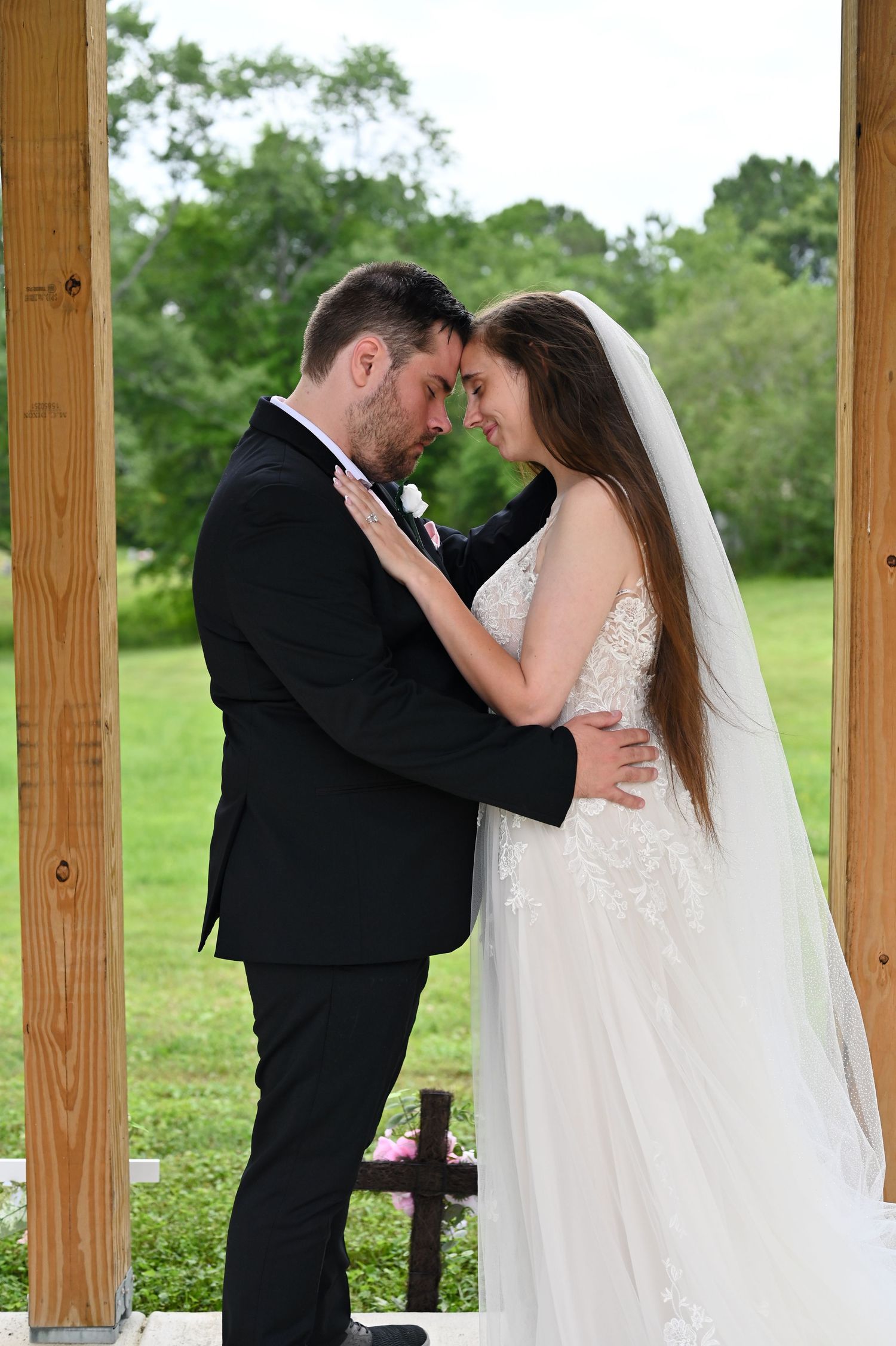 Bride and groom share an intimate forehead touch during outdoor wedding ceremony, bride in lace gown with veil.