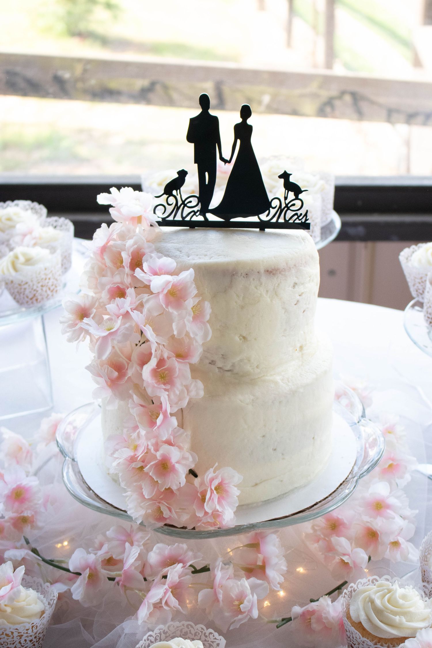 Two-tier white wedding cake with pink cherry blossoms and silhouette bride and groom cake topper with dogs.