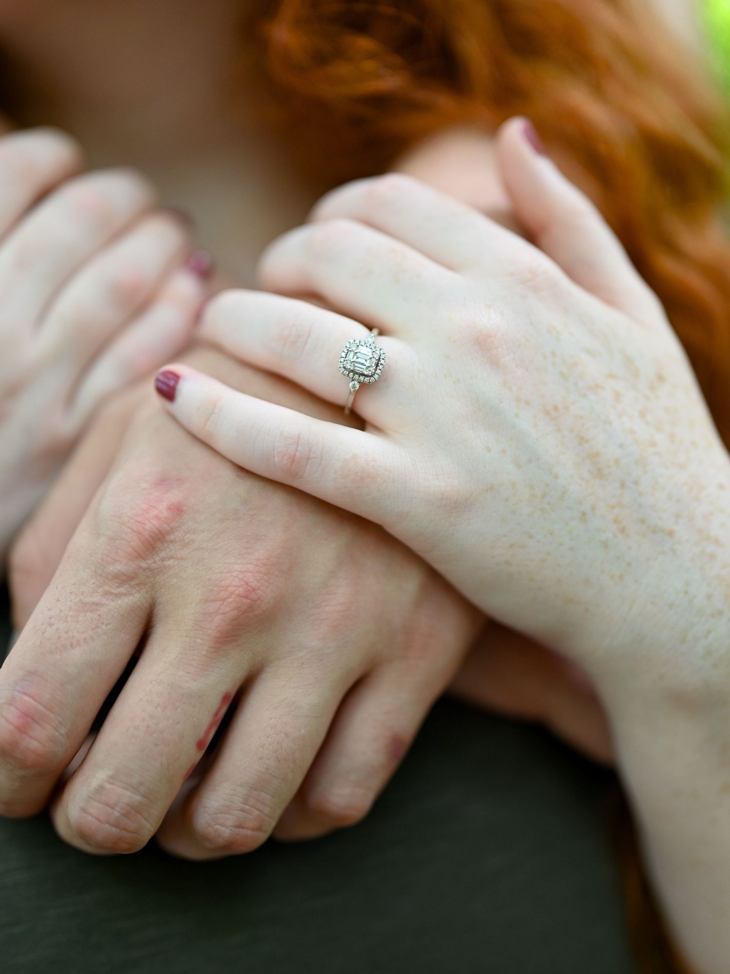 Close-up of a woman's hand wearing a diamond halo engagement ring, resting on another person's arm.