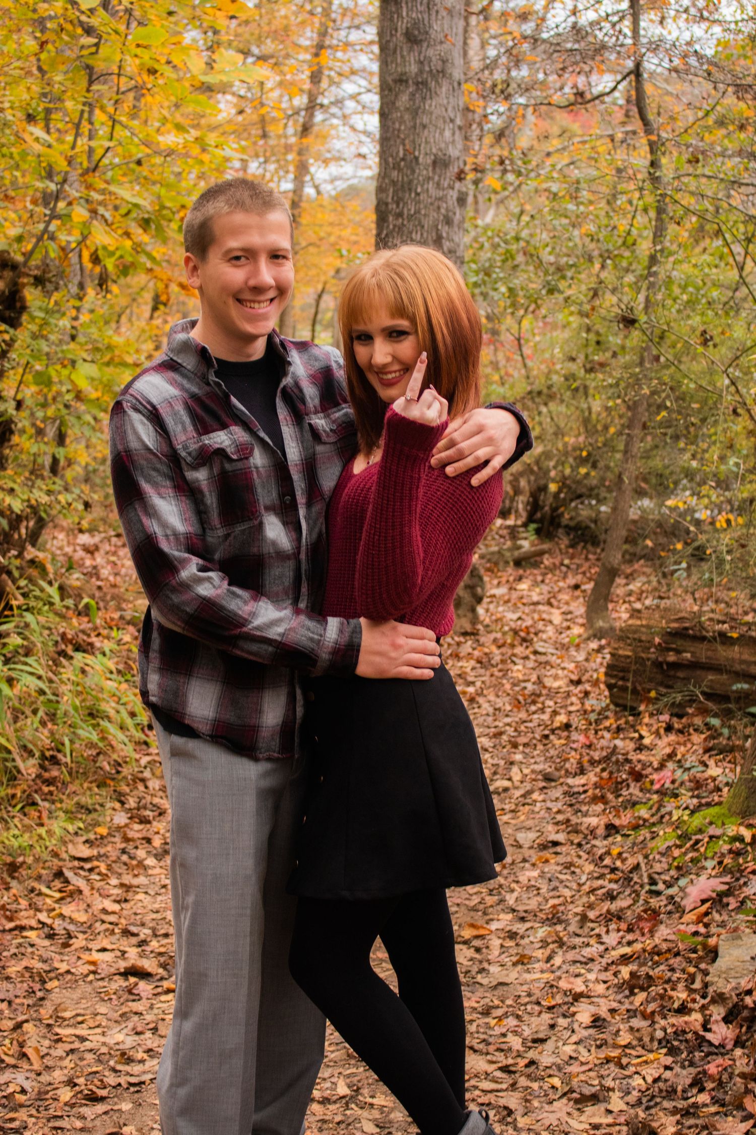 Couple embracing on a leaf-covered forest path surrounded by colorful autumn foliage.