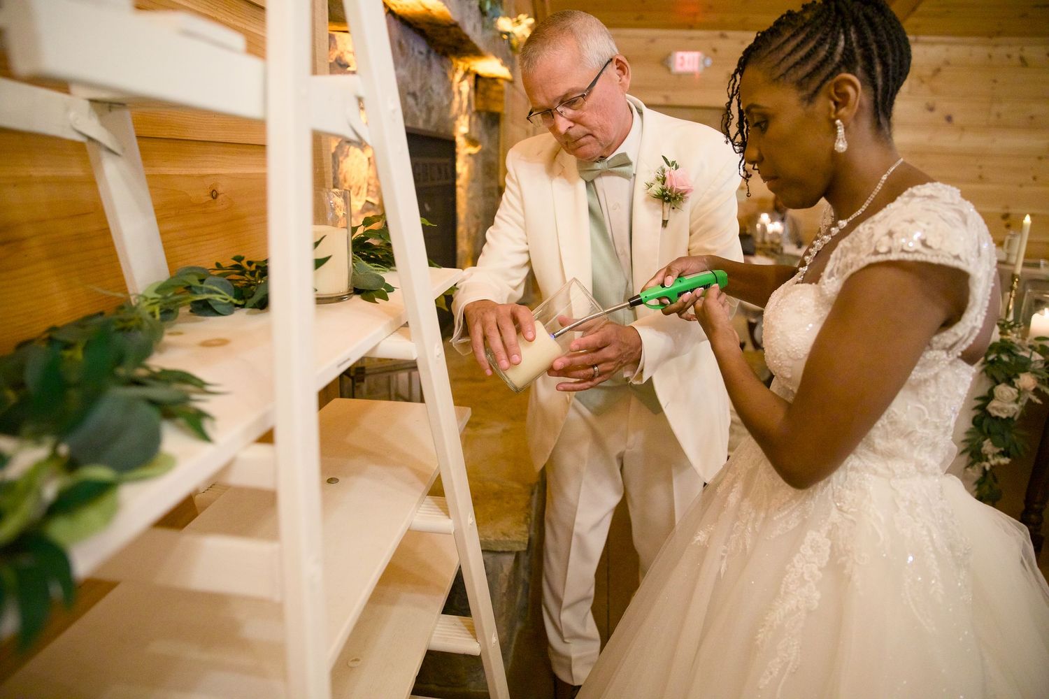 Bride and groom cutting wedding cake together at rustic barn wedding reception with white wooden shelving.
