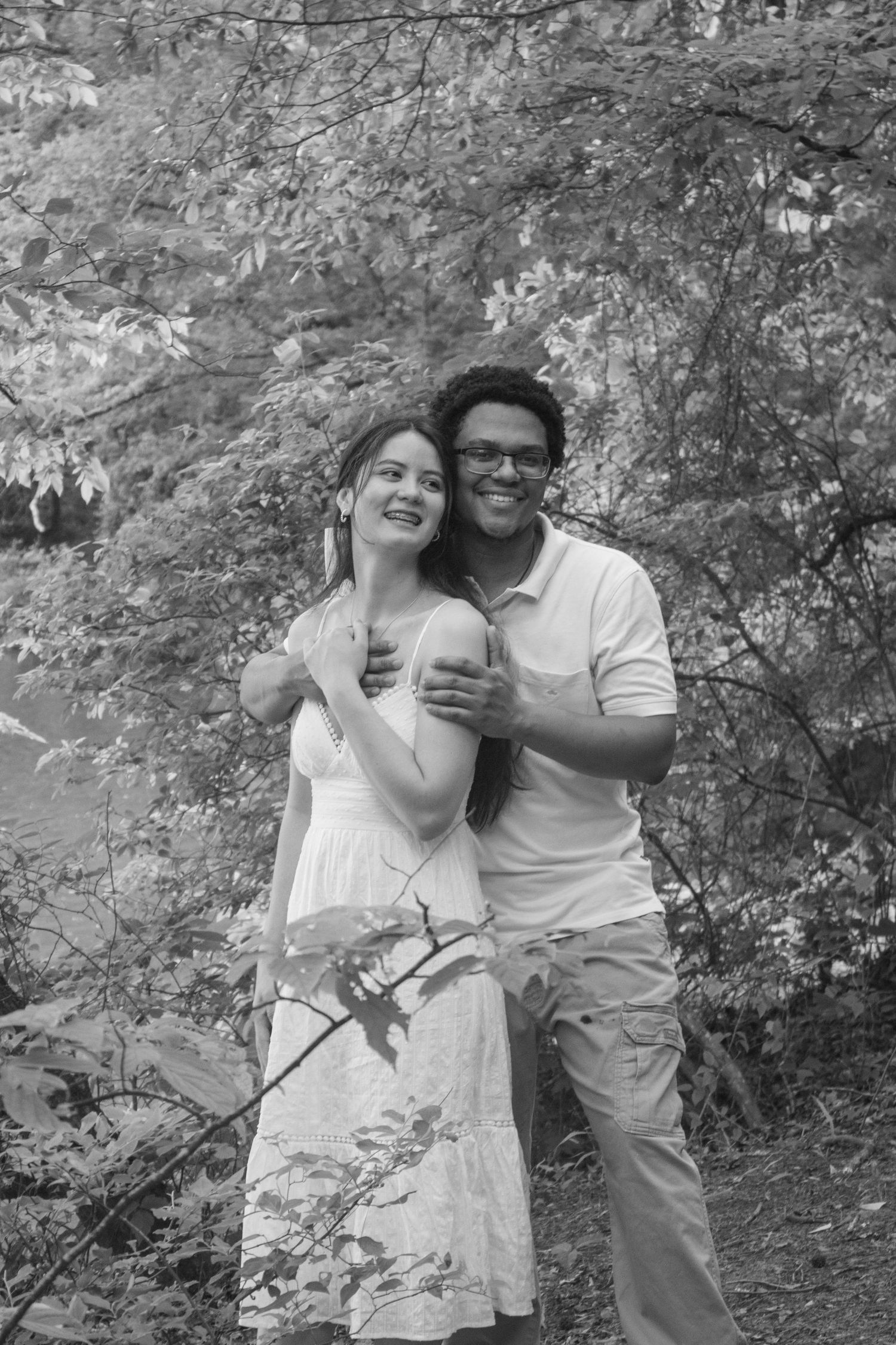 Happy couple embracing and smiling together outdoors among autumn foliage in black and white photo.