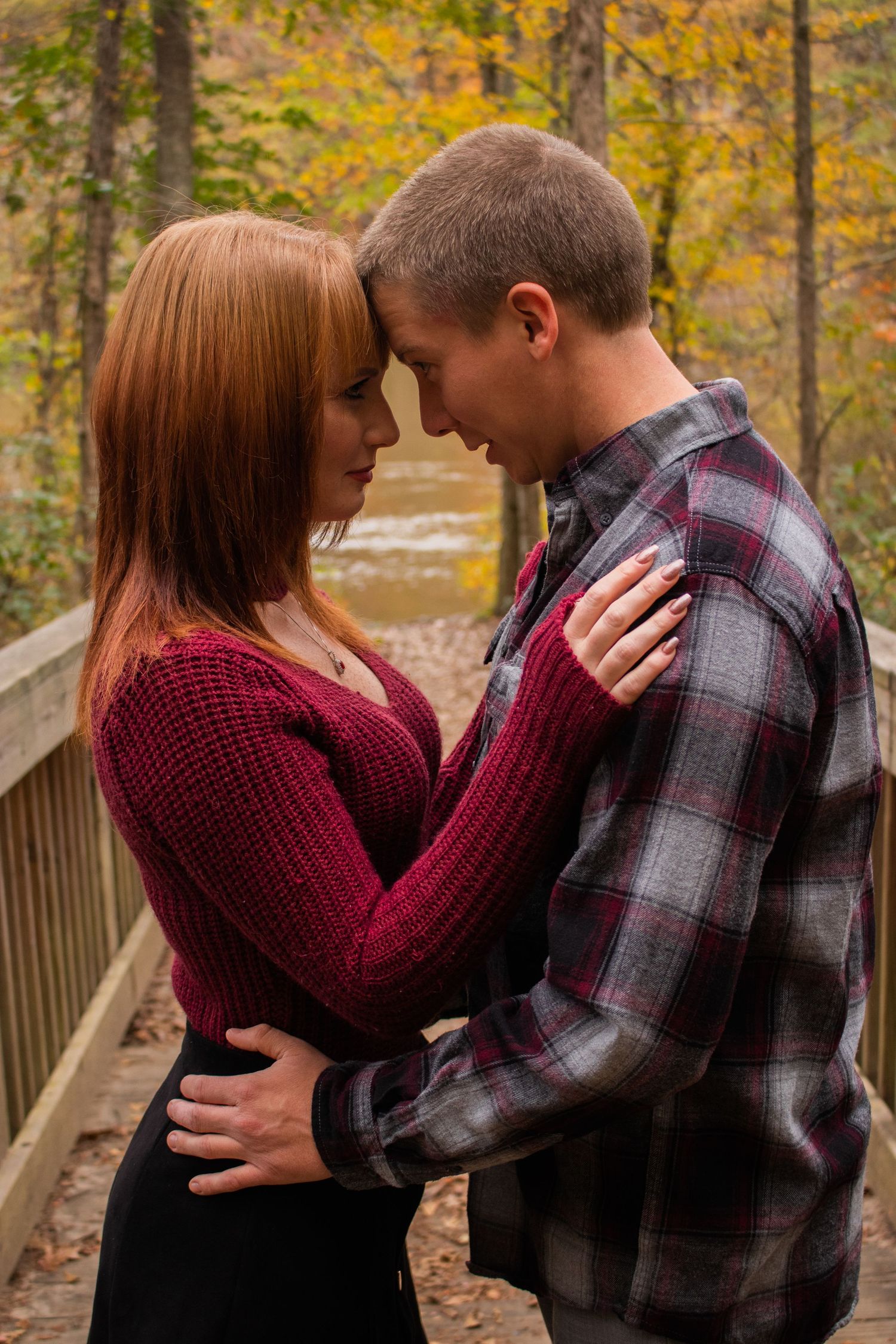 Couple sharing a romantic moment on a wooden bridge surrounded by colorful autumn foliage.