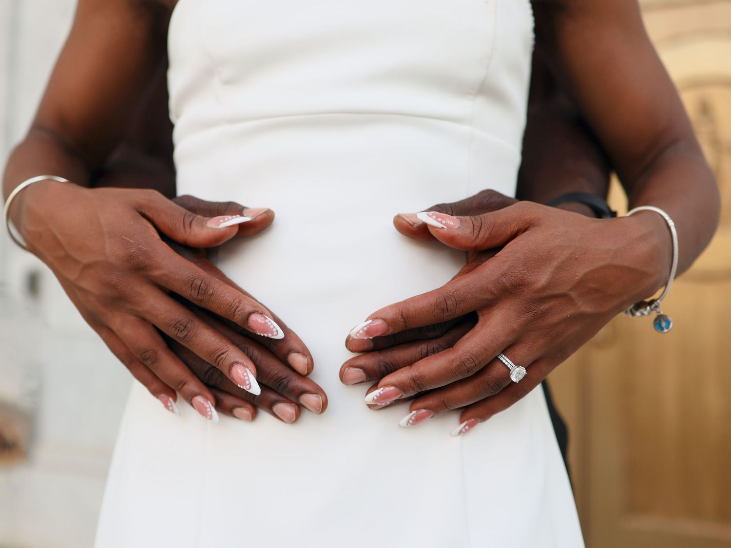Couple tenderly cradling pregnant belly, wearing wedding rings, dressed in white, showcasing maternity and love.