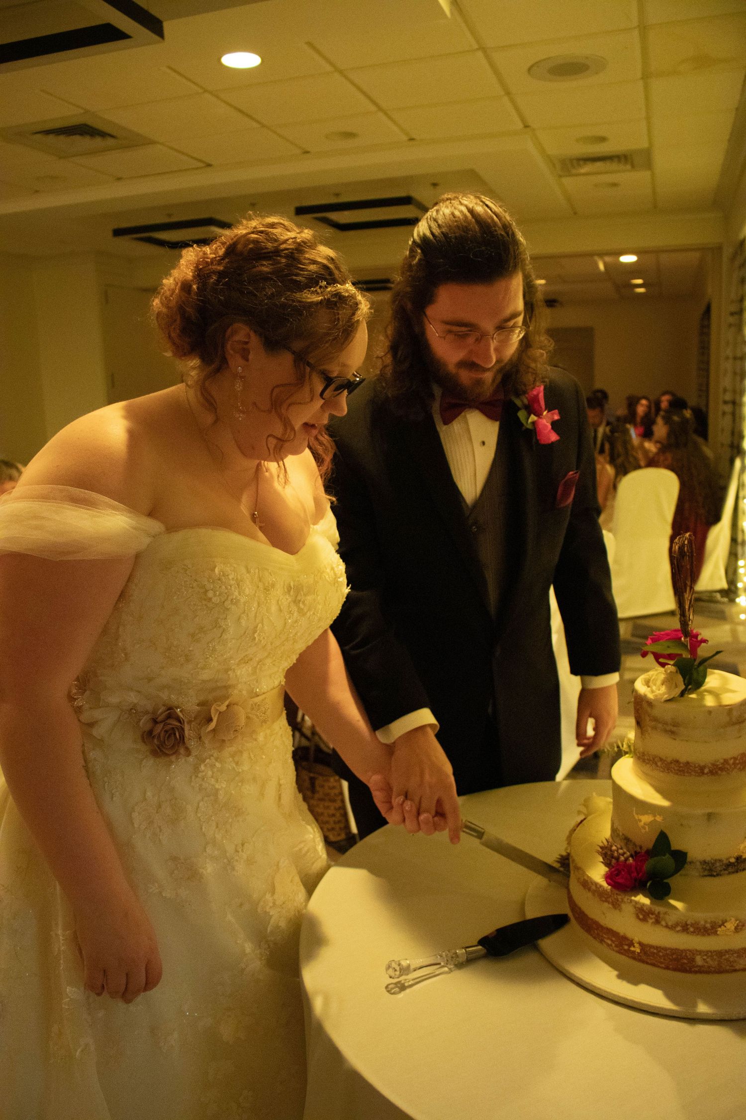 Bride and groom cutting wedding cake together at indoor reception venue.