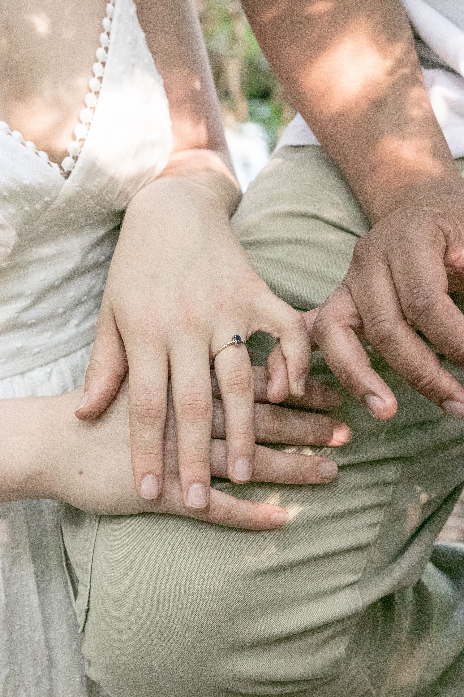 Close-up of engaged couple holding hands showing a delicate engagement ring outdoors.