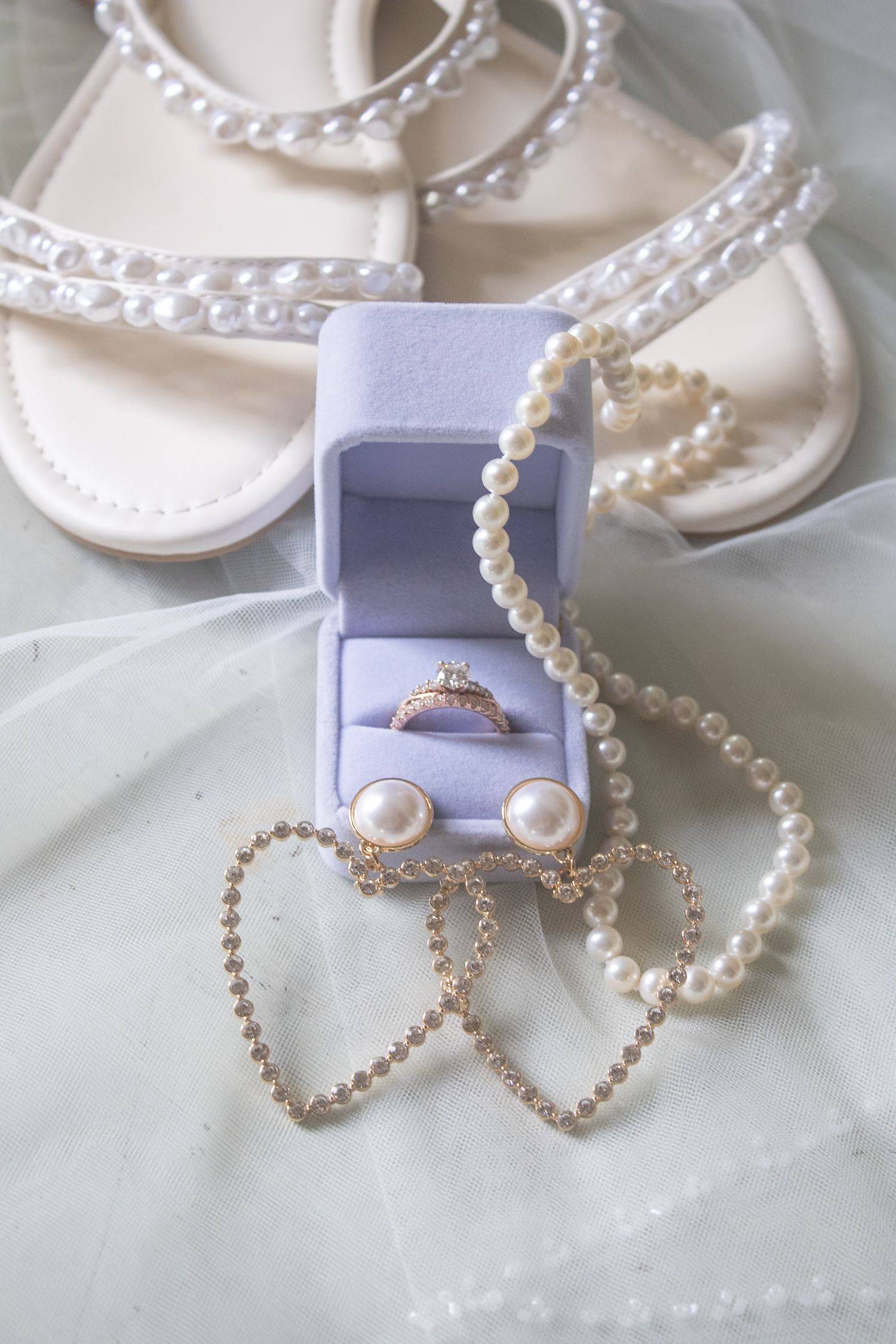 Bridal accessories flat lay with diamond ring in blue box, pearl necklace, earrings, and pearl sandals.