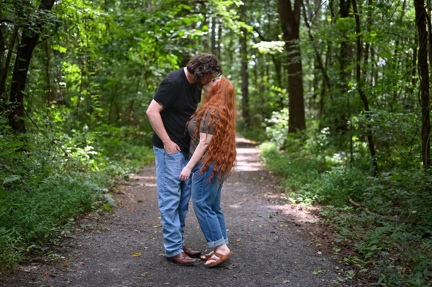 Couple sharing a romantic moment on a forest path surrounded by lush green trees.