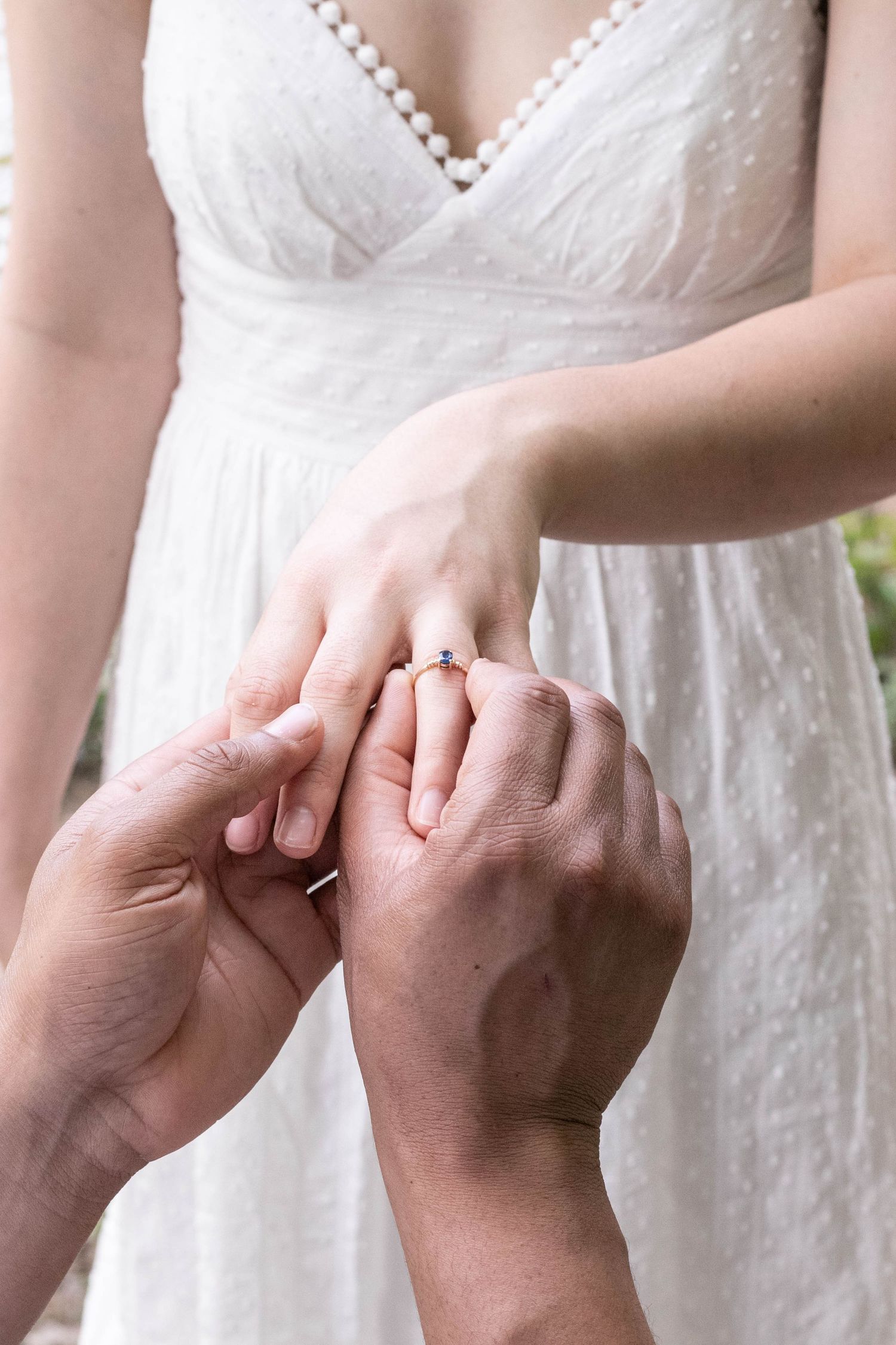 Groom carefully placing a blue sapphire diamond ring on bride's finger during wedding ceremony.
