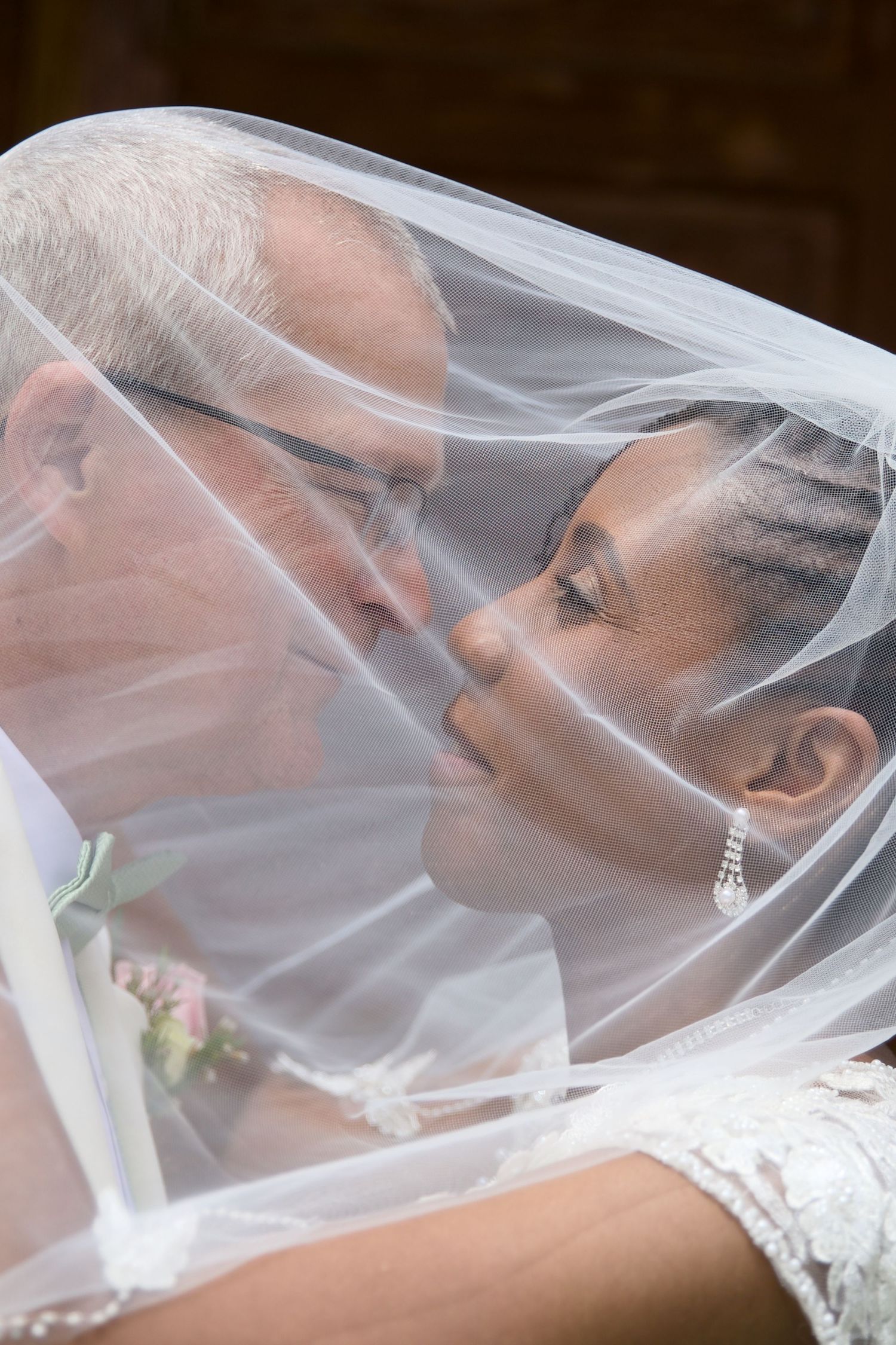 Interracial newlywed couple sharing a romantic kiss under the bride's white wedding veil.