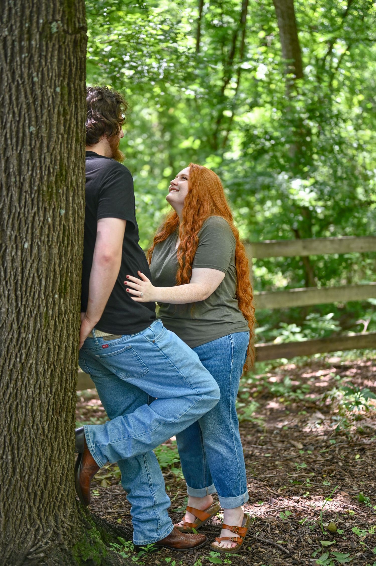 Couple sharing a romantic moment leaning against a tree in a lush green forest.
