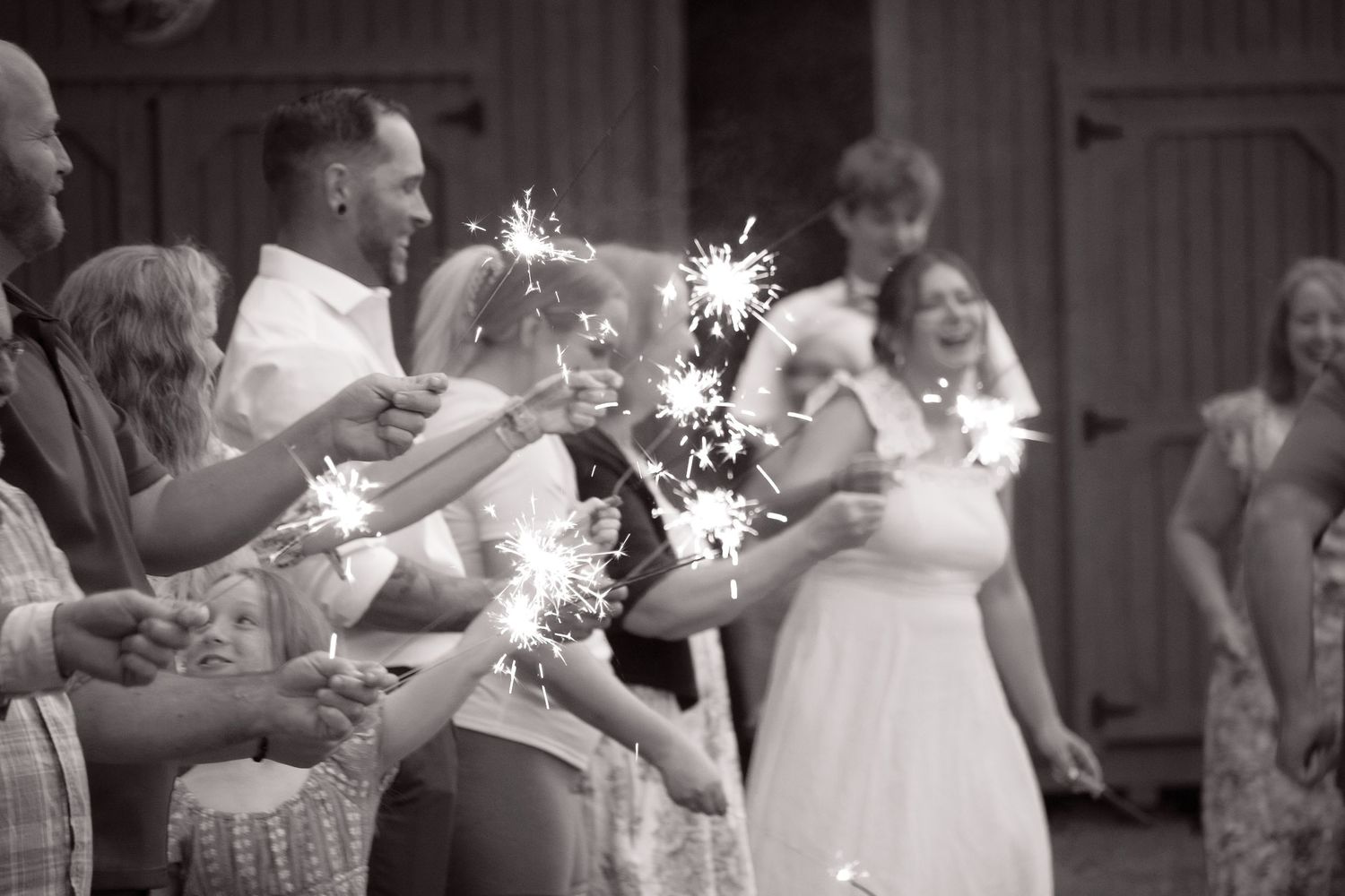 Black and white wedding photo of guests holding sparklers during a romantic outdoor celebration ceremony.