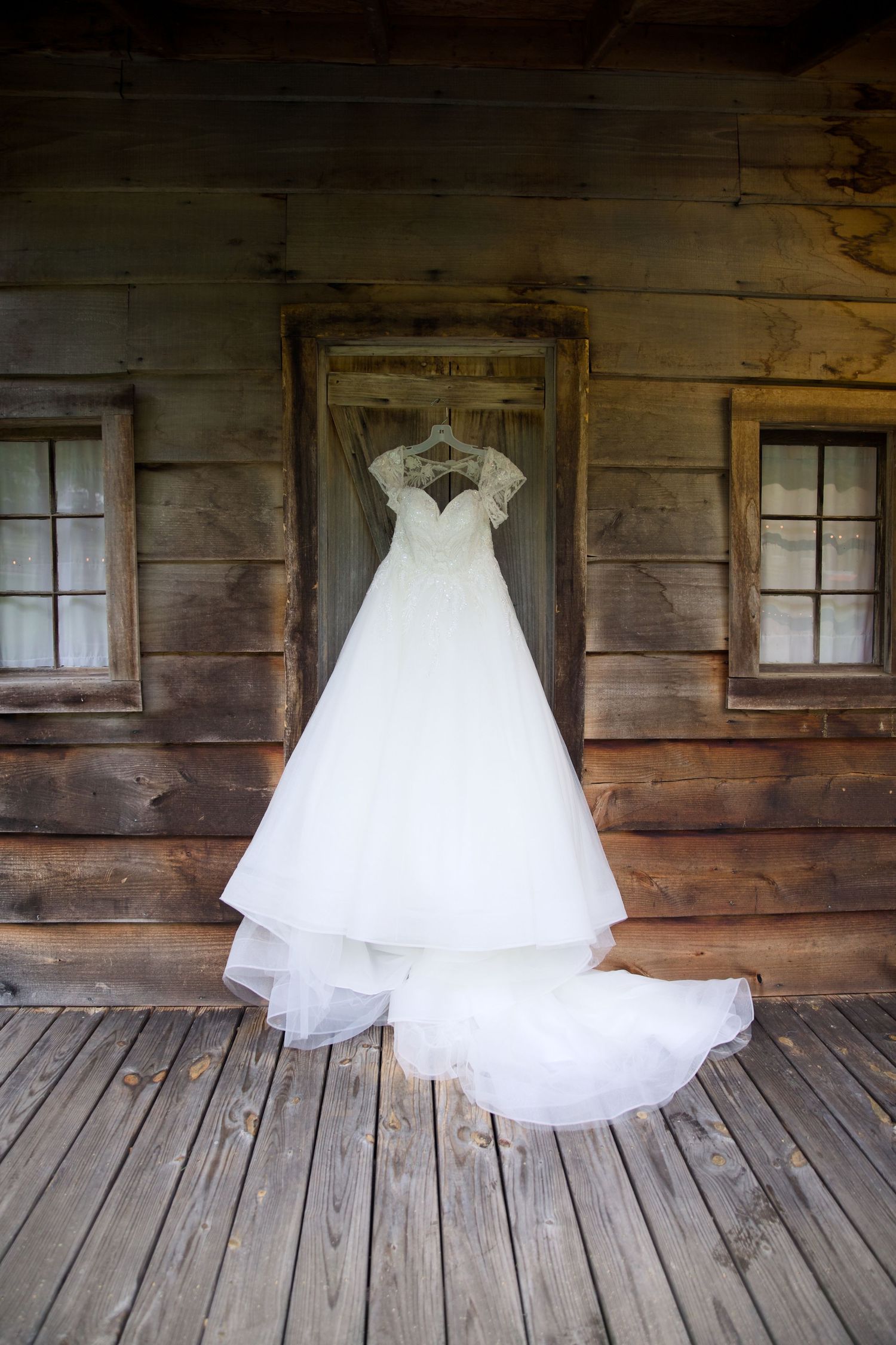 White ball gown wedding dress with lace bodice and long train hanging on rustic wooden cabin porch.