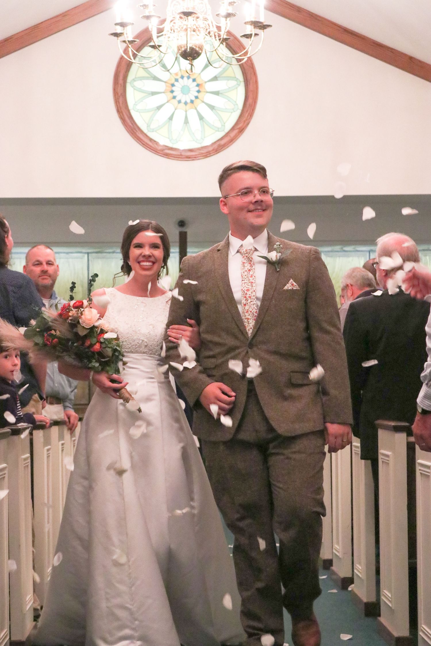 Joyful newlyweds walk down church aisle as guests toss white flower petals in celebration.