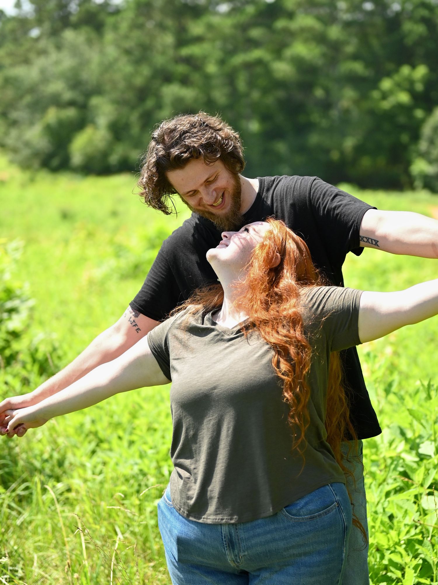 Joyful couple dancing in a sunny green meadow, woman with long red hair spreads her arms wide.