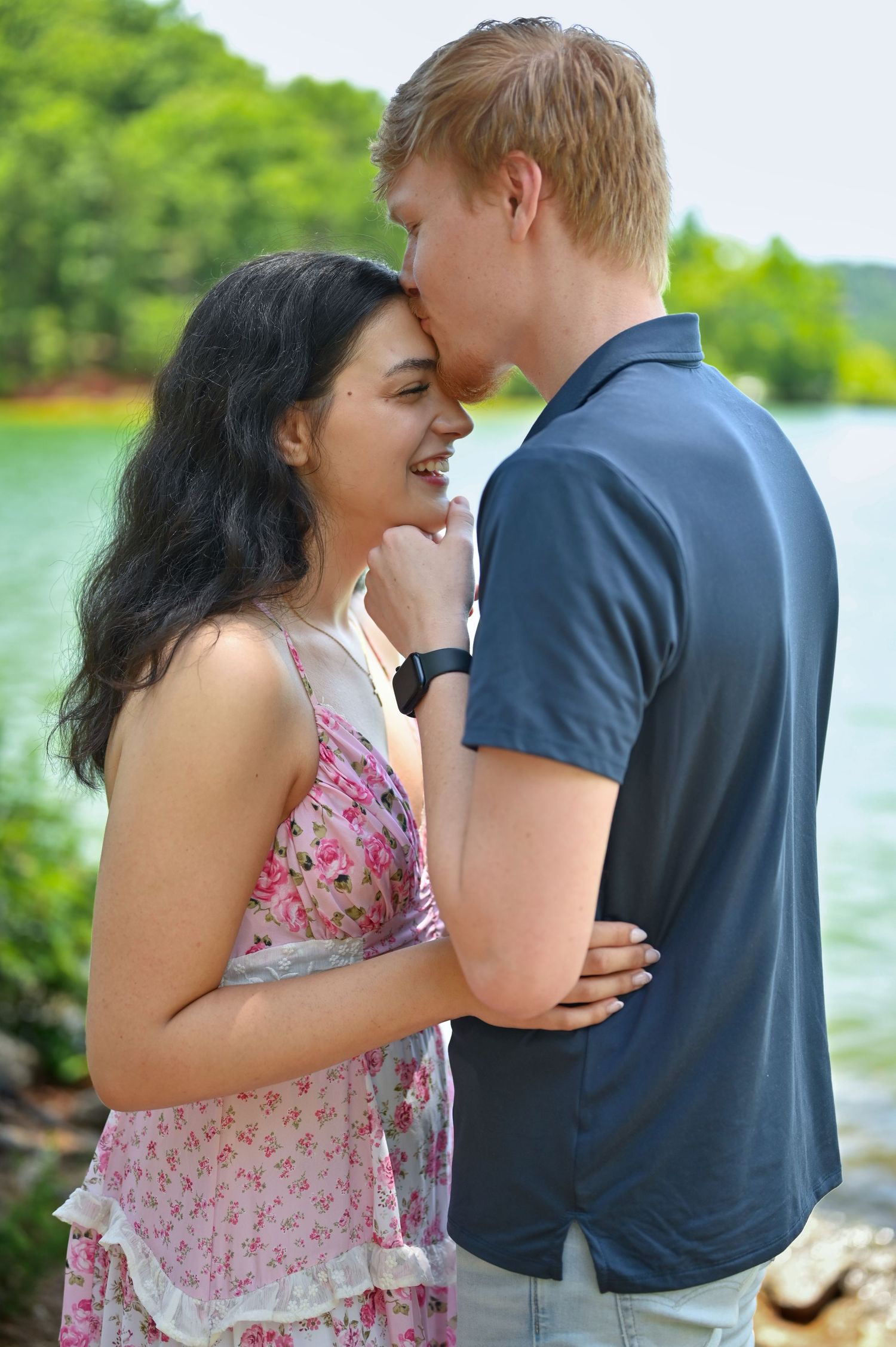 A happy young interracial couple sharing a romantic moment near a scenic lakeside, the woman in a floral dress.