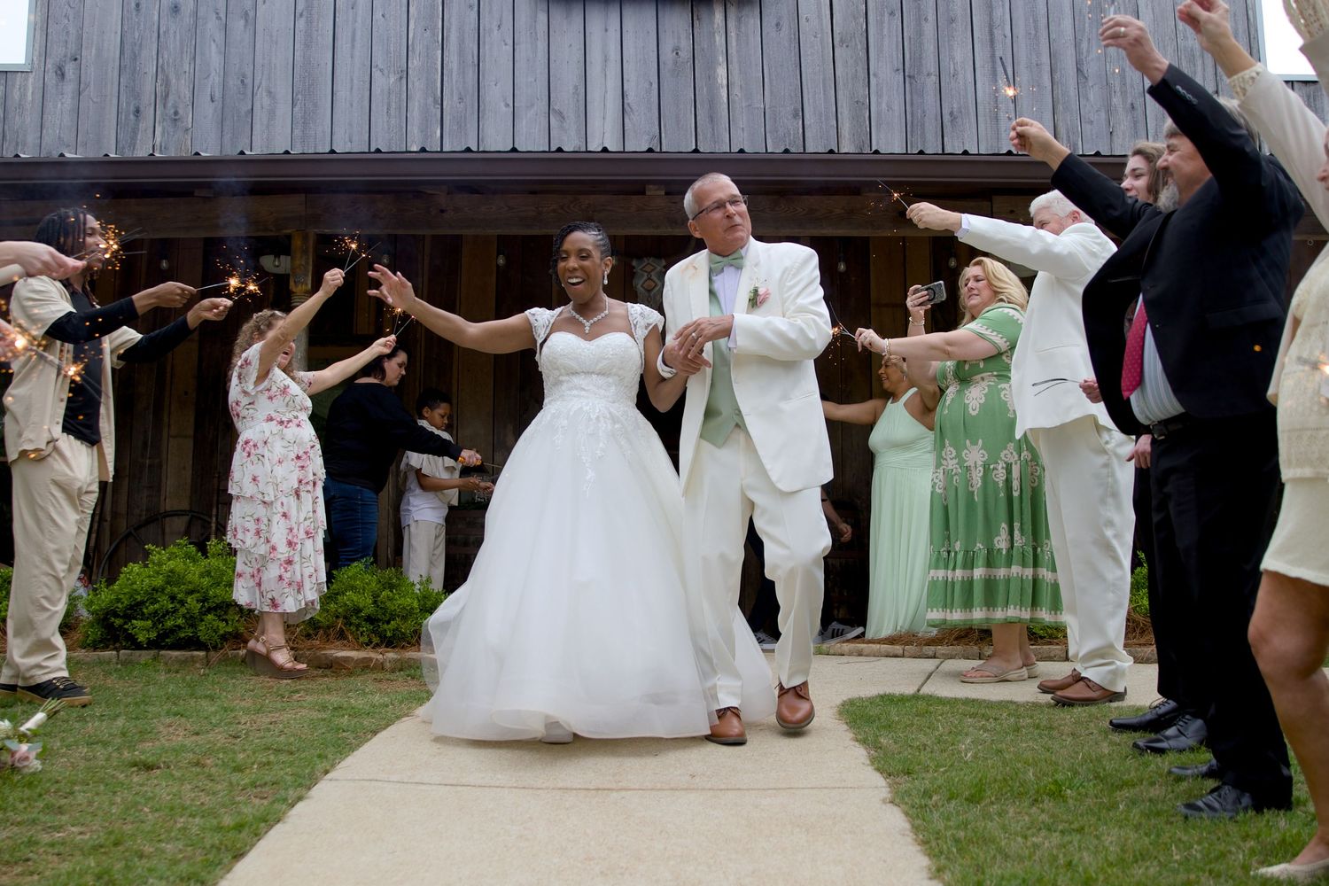 Newlywed couple exits wedding venue through sparkler send-off with guests celebrating outdoors.