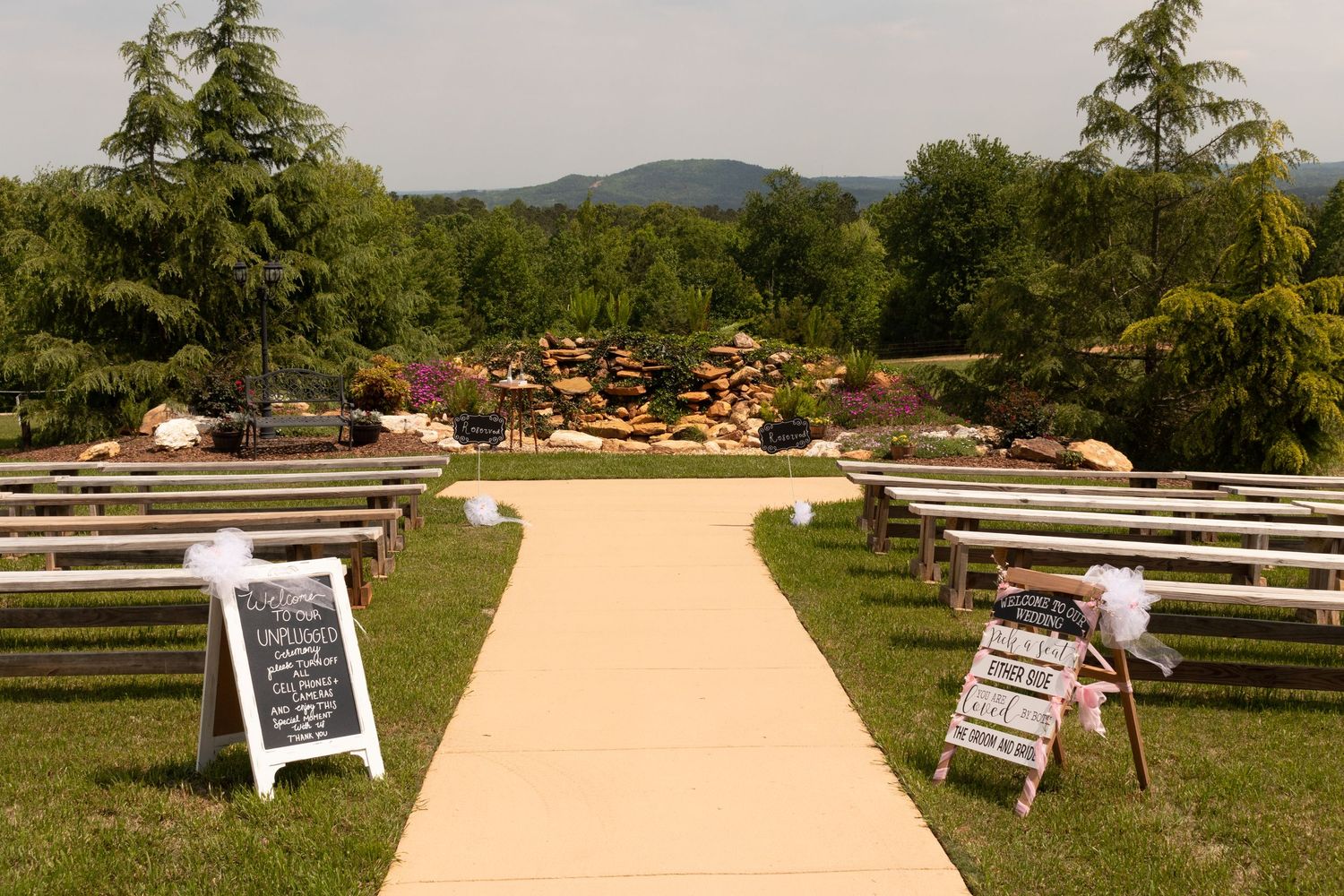 Elegant outdoor wedding ceremony setup with white aisle runner, wooden benches, and mountain views.