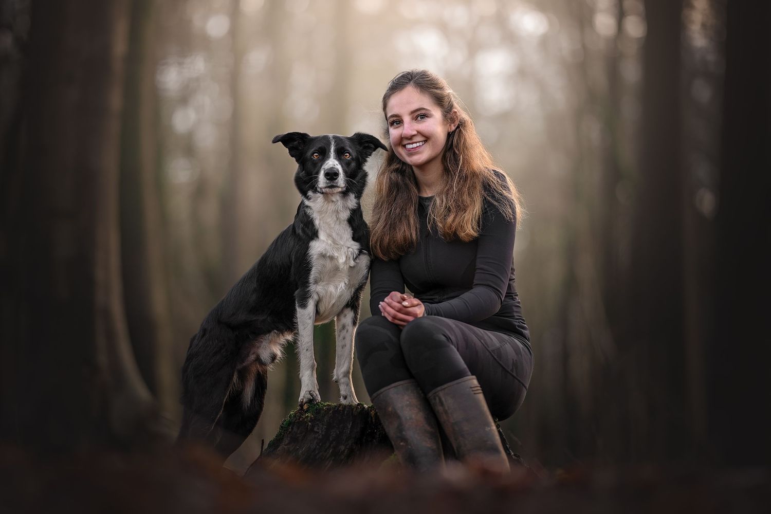 a portrait of an owner and her dog, sat on a log together in a woodland in wiltshire